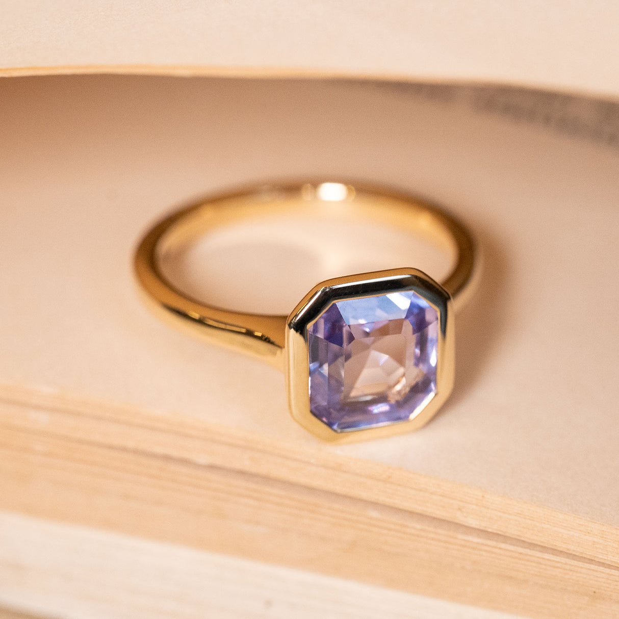 Antique-inspired emerald-cut lavender sapphire engagement ring set in a refined yellow gold bezel setting.