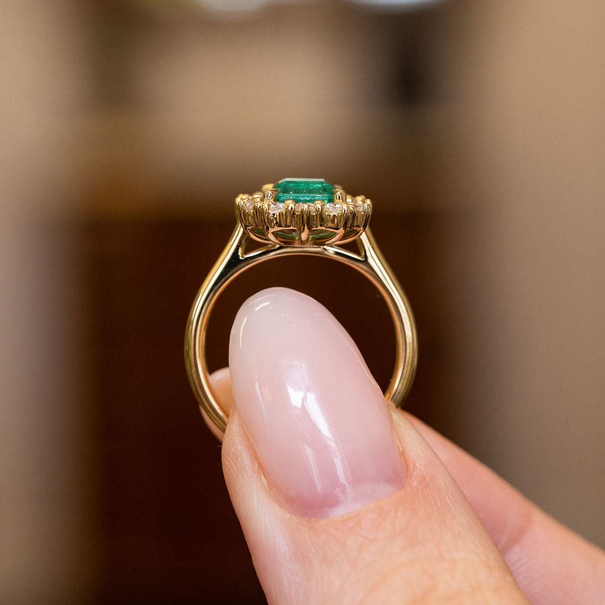 Antique-inspired emerald and diamond cluster engagement ring displaying an emerald-cut emerald and diamond halo in yellow gold.