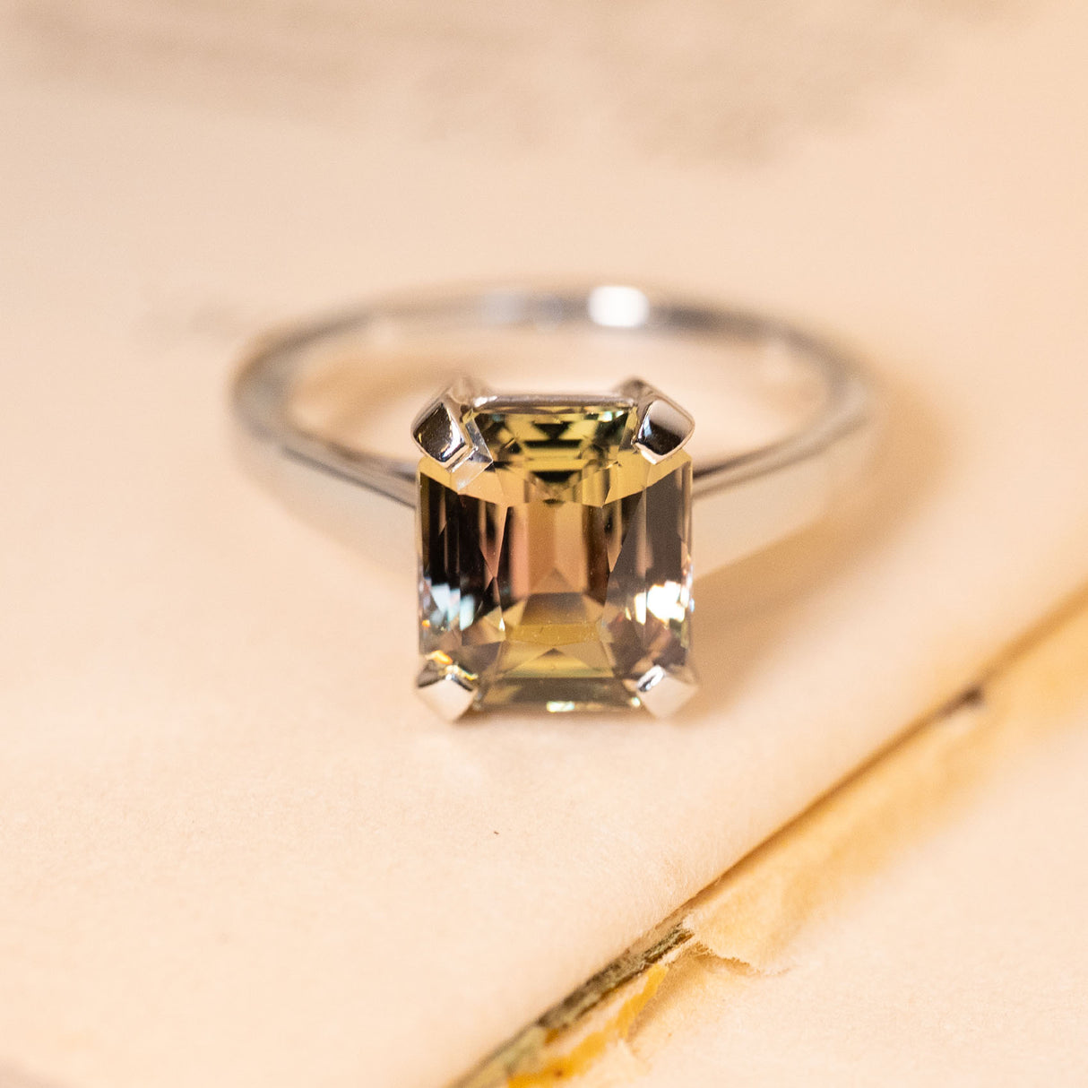 Green and brown colour-change sapphire solitaire engagement ring featuring an emerald-cut sapphire in a four-claw white gold setting.