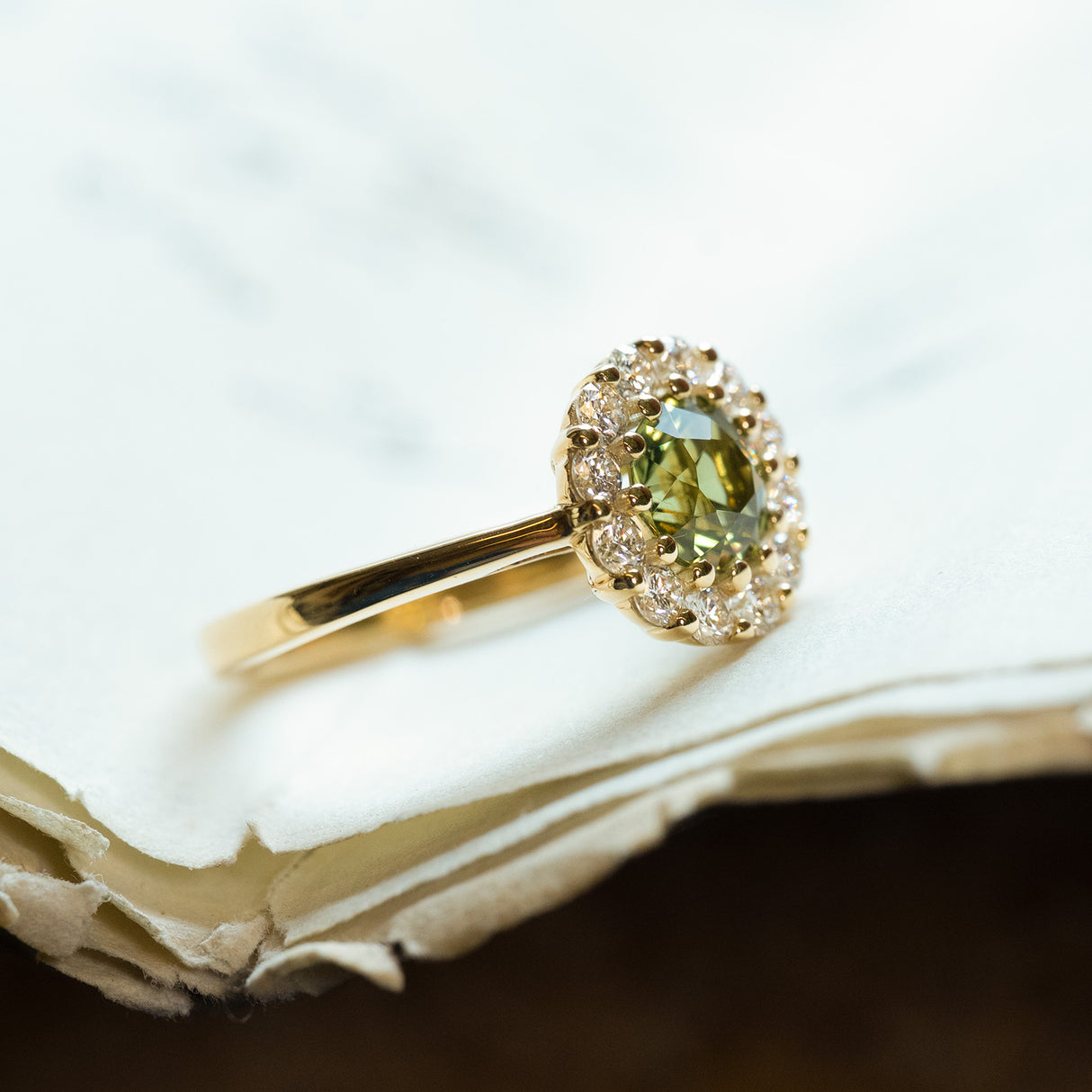 Green sapphire and diamond cluster engagement ring with yellow gold band and diamond halo.
