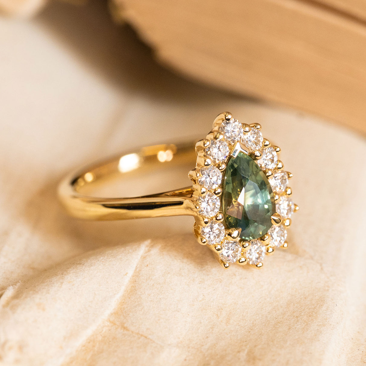 Pear-cut green sapphire and diamond cluster engagement ring with a vivid green sapphire framed by brilliant-cut diamonds in yellow gold.