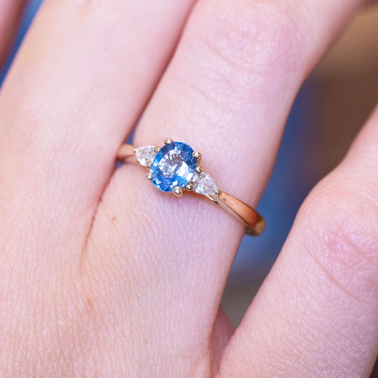 Light blue sapphire and diamond three-stone engagement ring with diamond side stones and gold band.