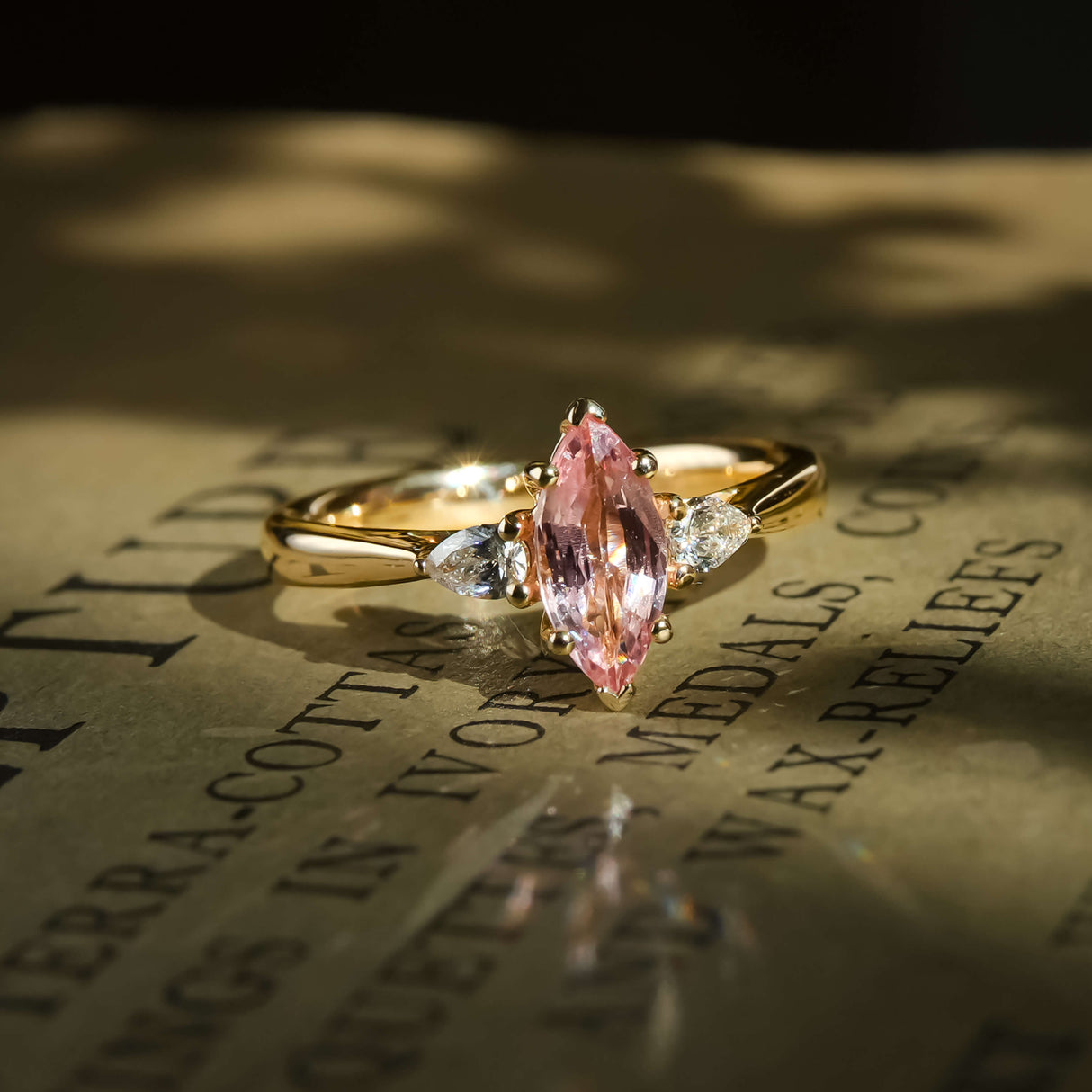 marquise pink sapphire three stone engagement ring with diamond side stones in yellow gold