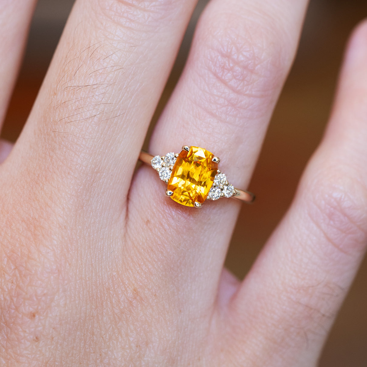 Orange cushion-cut sapphire and diamond cluster trefoil ring showing gemstone and setting detail.