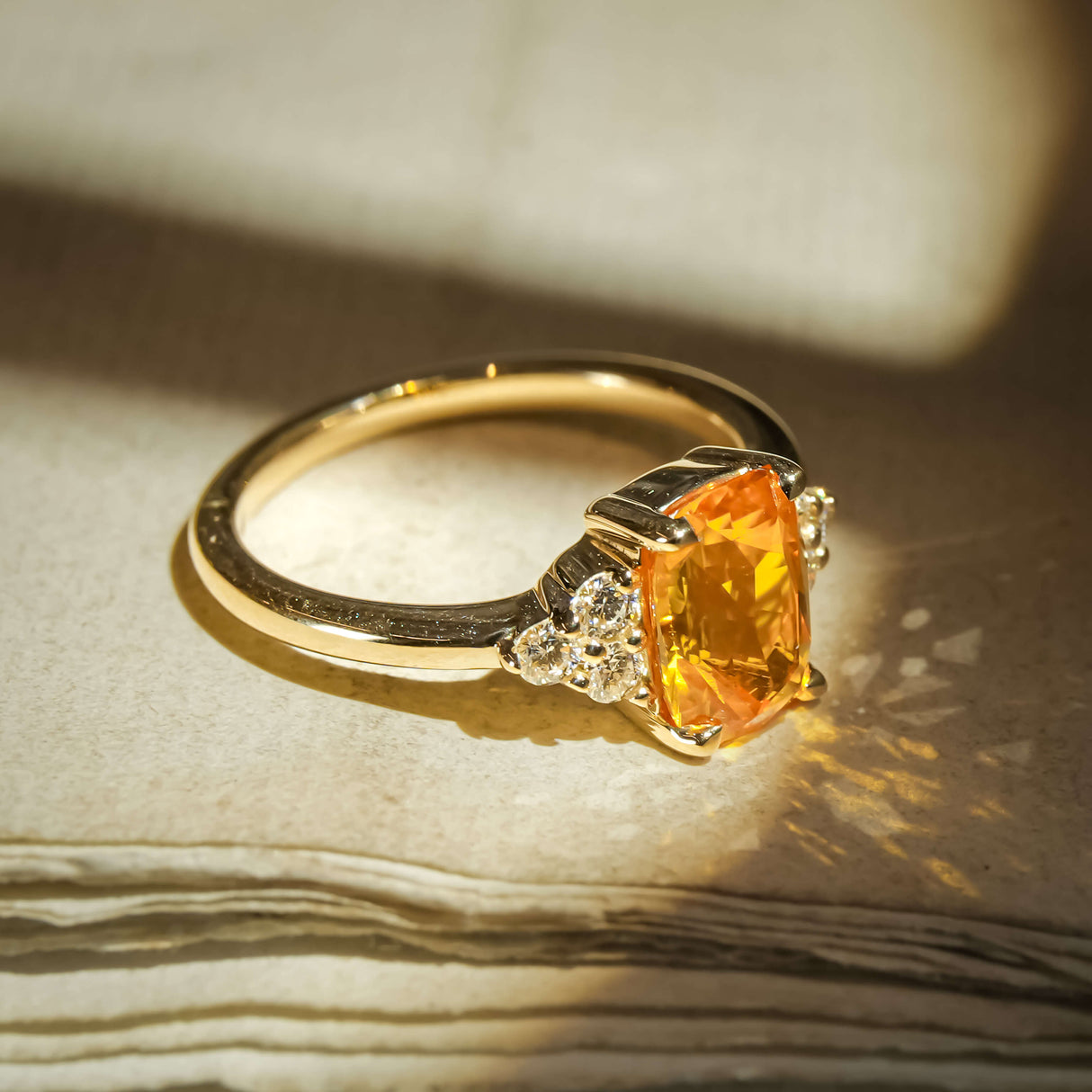 Orange sapphire ring with cushion cut gemstone and diamond trefoil cluster in gold