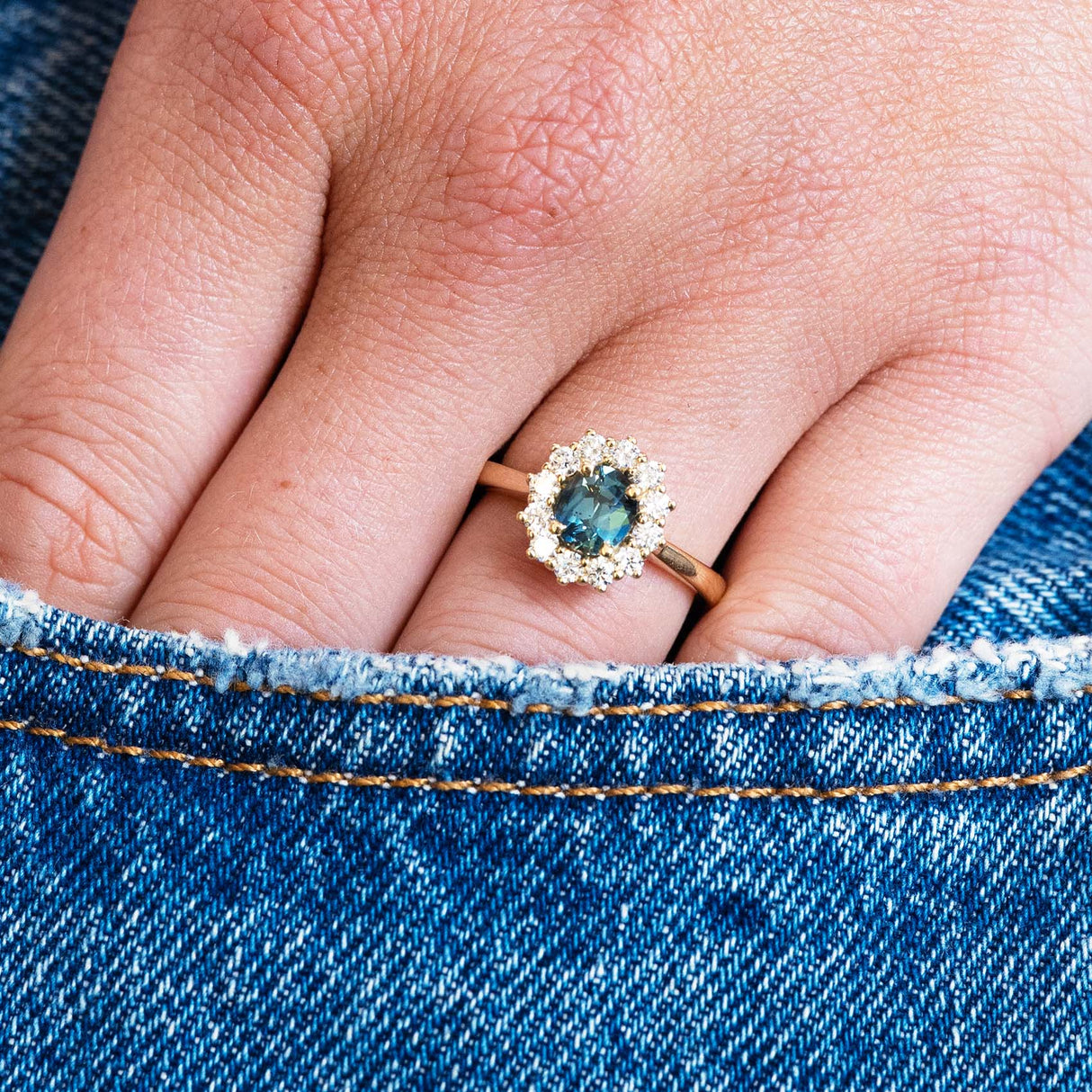 Teal sapphire ring worn on hand with denim pocket detail.