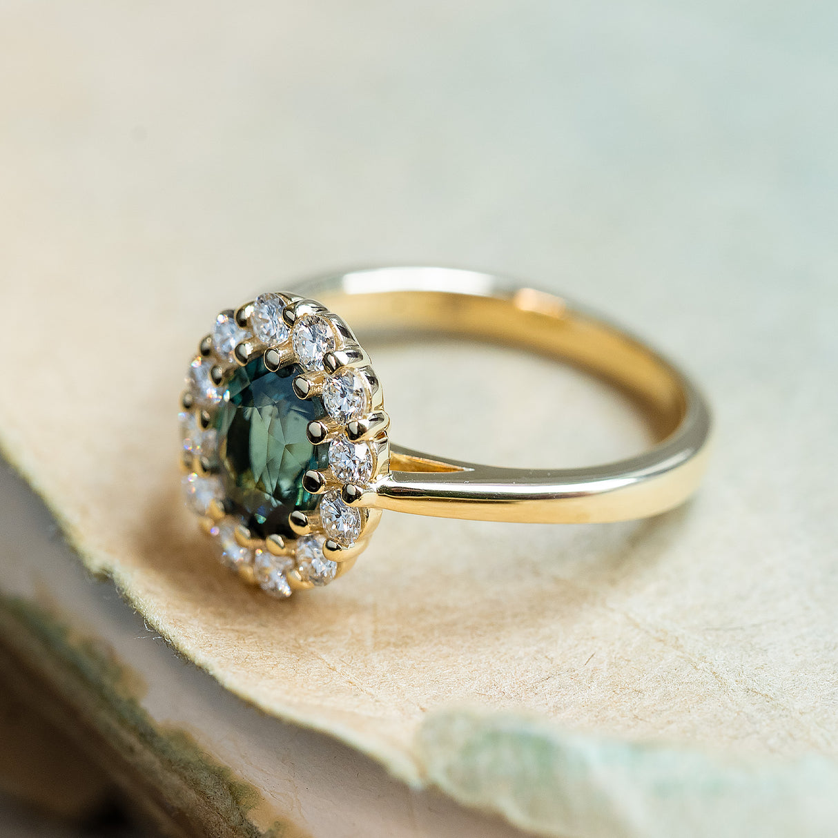 Antique inspired green sapphire engagement ring with oval sapphire centre and diamond cluster surround.