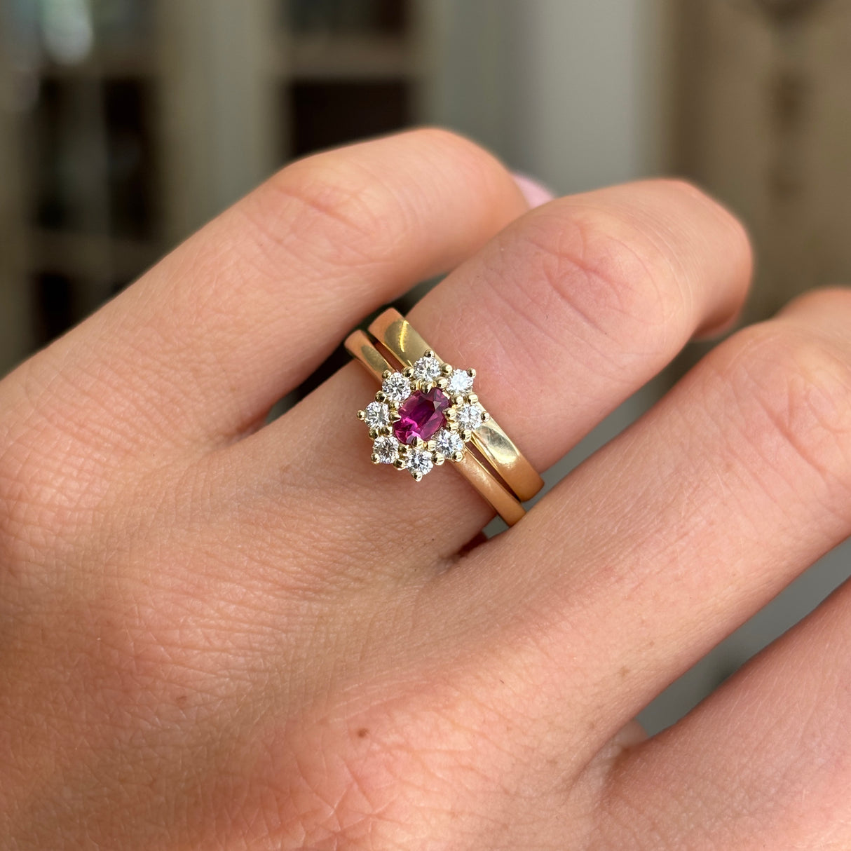 Antique-inspired yellow gold ruby cluster ring worn on hand, featuring an oval-cut ruby surrounded by diamonds, photographed to highlight the classic cluster design and fine craftsmanship.