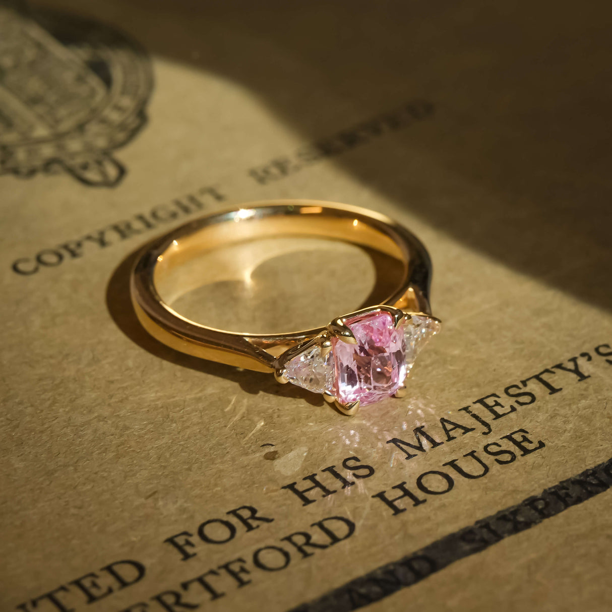 Padparadscha sapphire and diamond three stone engagement ring in yellow gold band