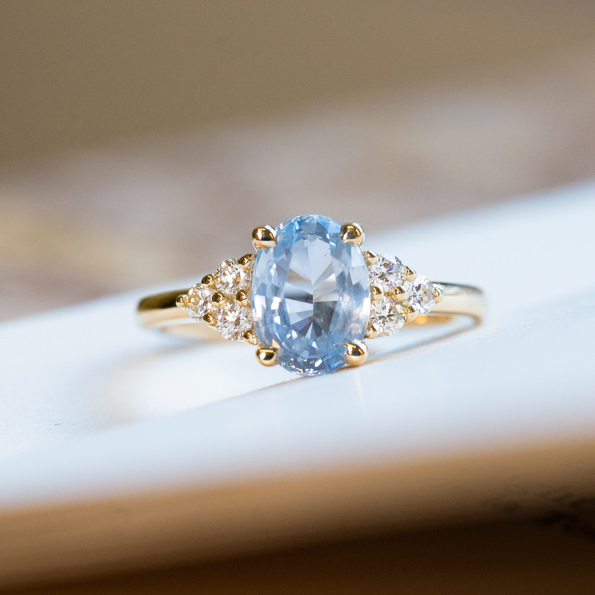 Pale blue sapphire and diamond cluster tre-foil engagement ring with oval sapphire and diamond-set shoulders.