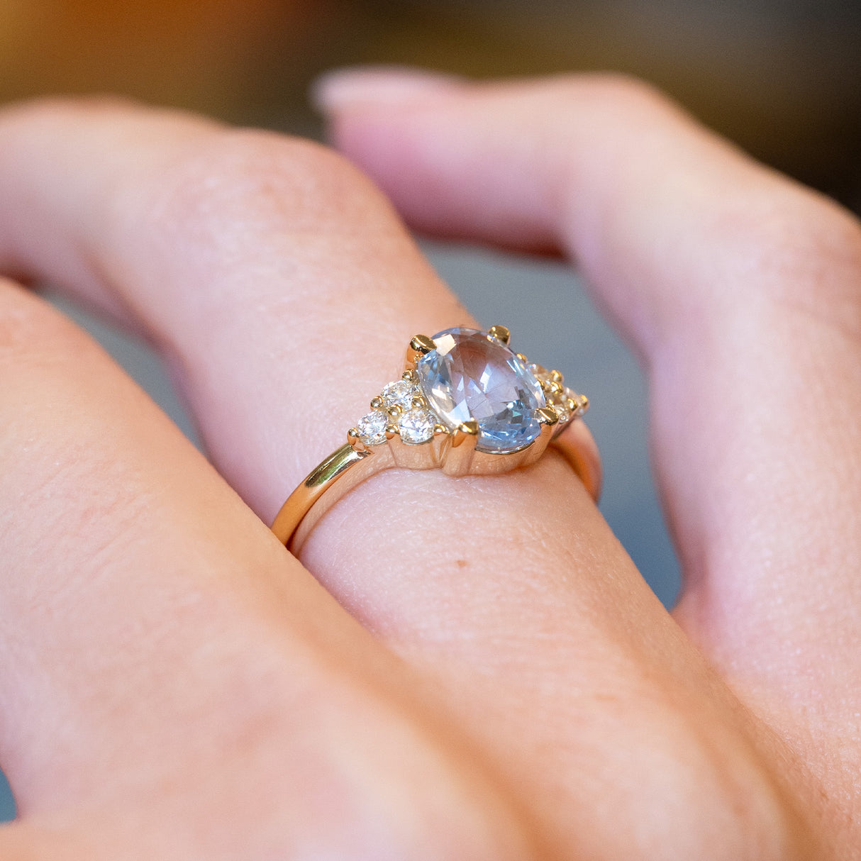 Pale blue sapphire and diamond cluster tre-foil engagement ring with oval sapphire in polished gold setting.