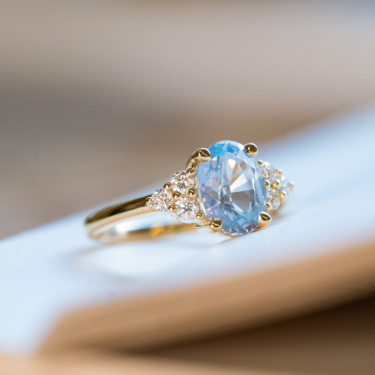 Pale blue sapphire and diamond cluster tre-foil engagement ring with oval sapphire in polished gold setting.