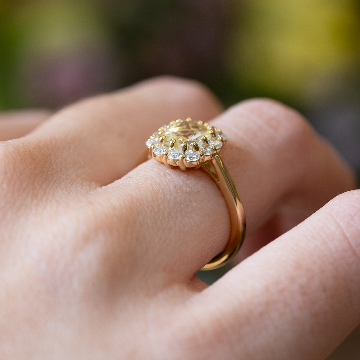 Pale yellow sapphire and diamond cluster engagement ring with delicate gold band and raised setting.