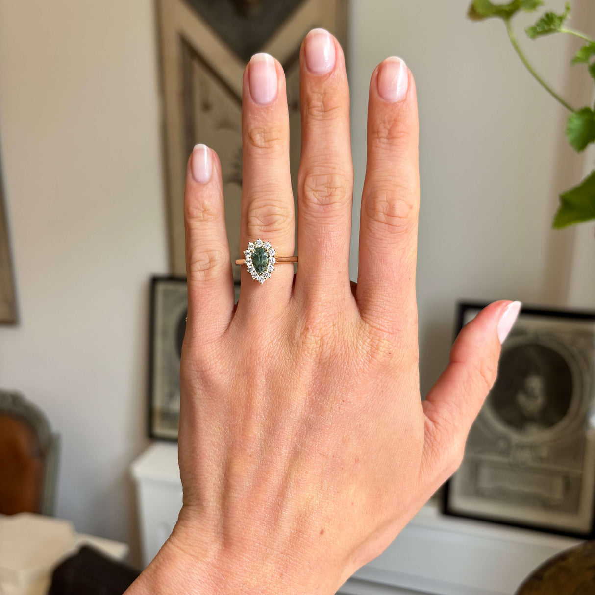 Antique-inspired green sapphire and diamond cluster ring in yellow gold worn on hand, showcasing the elegant pear-shaped centre stone and sparkling diamond halo in natural light.