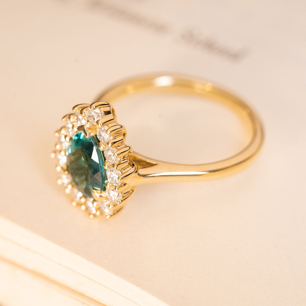 Pear-cut teal tourmaline and diamond cluster engagement ring in polished yellow gold