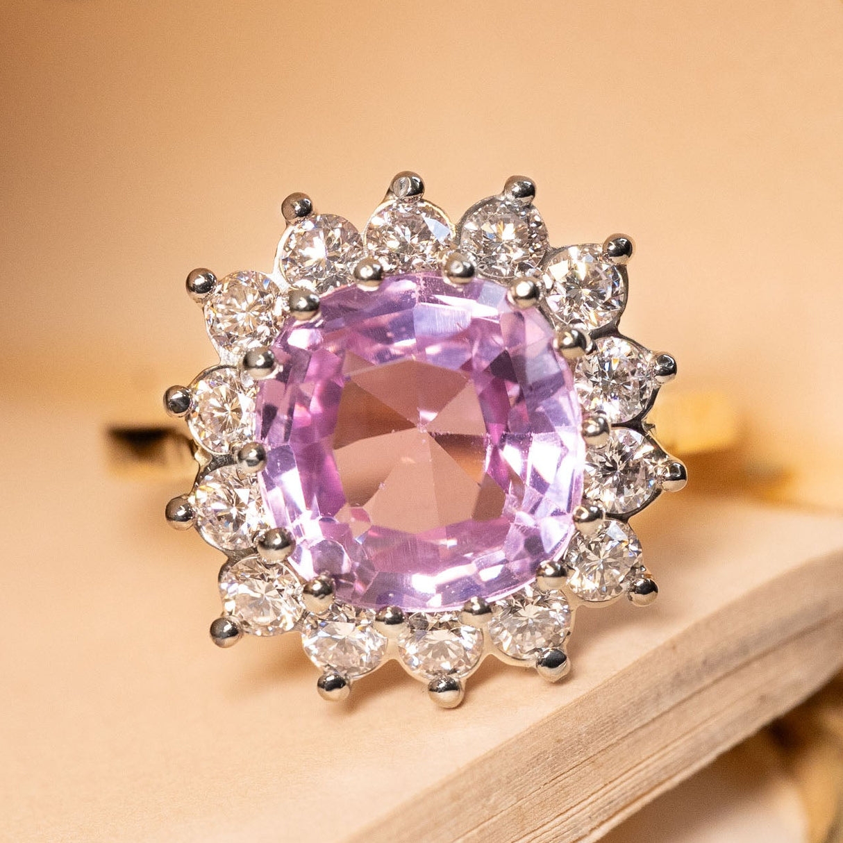 Pink Ceylon sapphire and diamond cluster engagement ring featuring a pastel pink cushion-cut sapphire surrounded by a sparkling halo of round brilliant-cut diamonds.