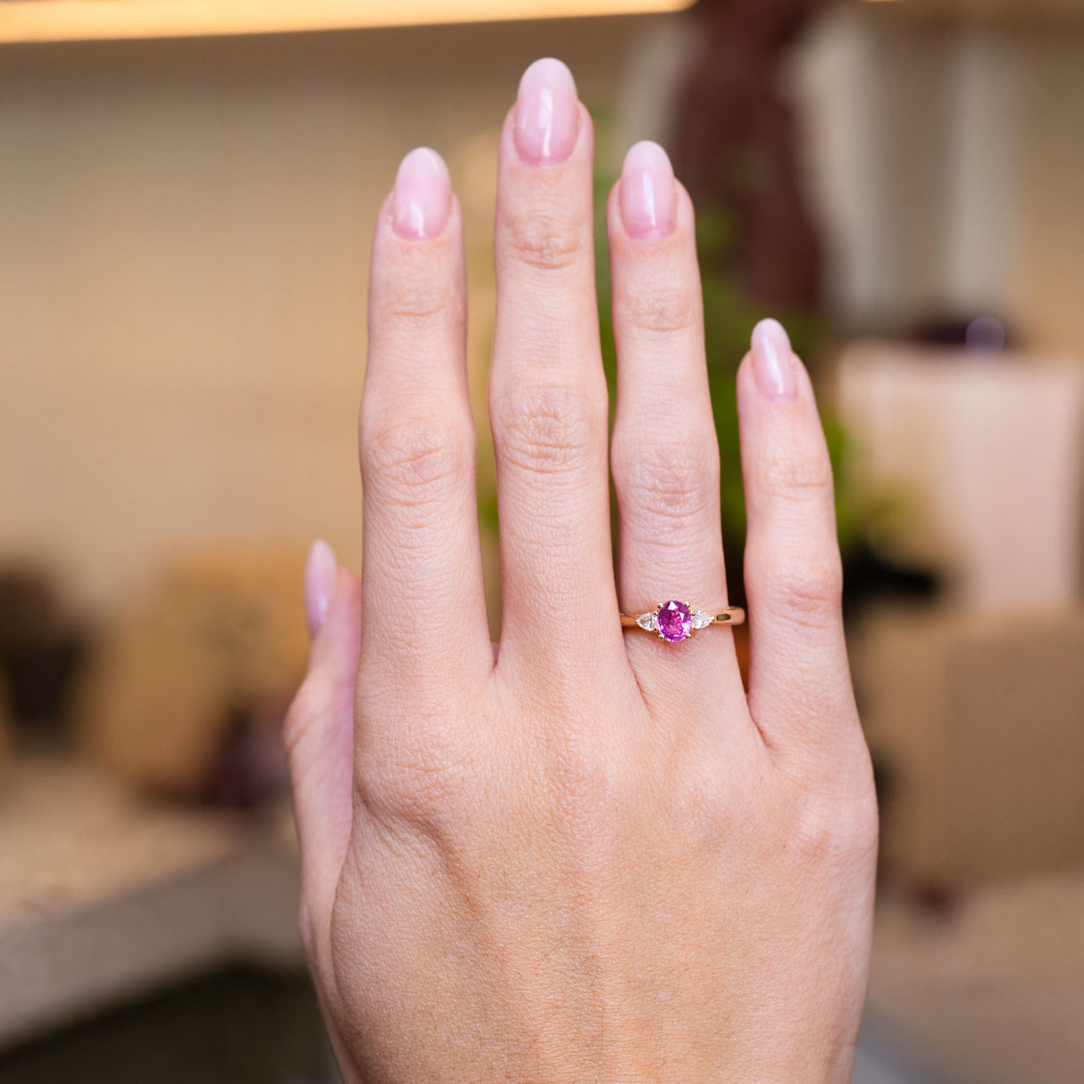 Pink oval sapphire and diamond three-stone engagement ring worn on hand with gold band.
