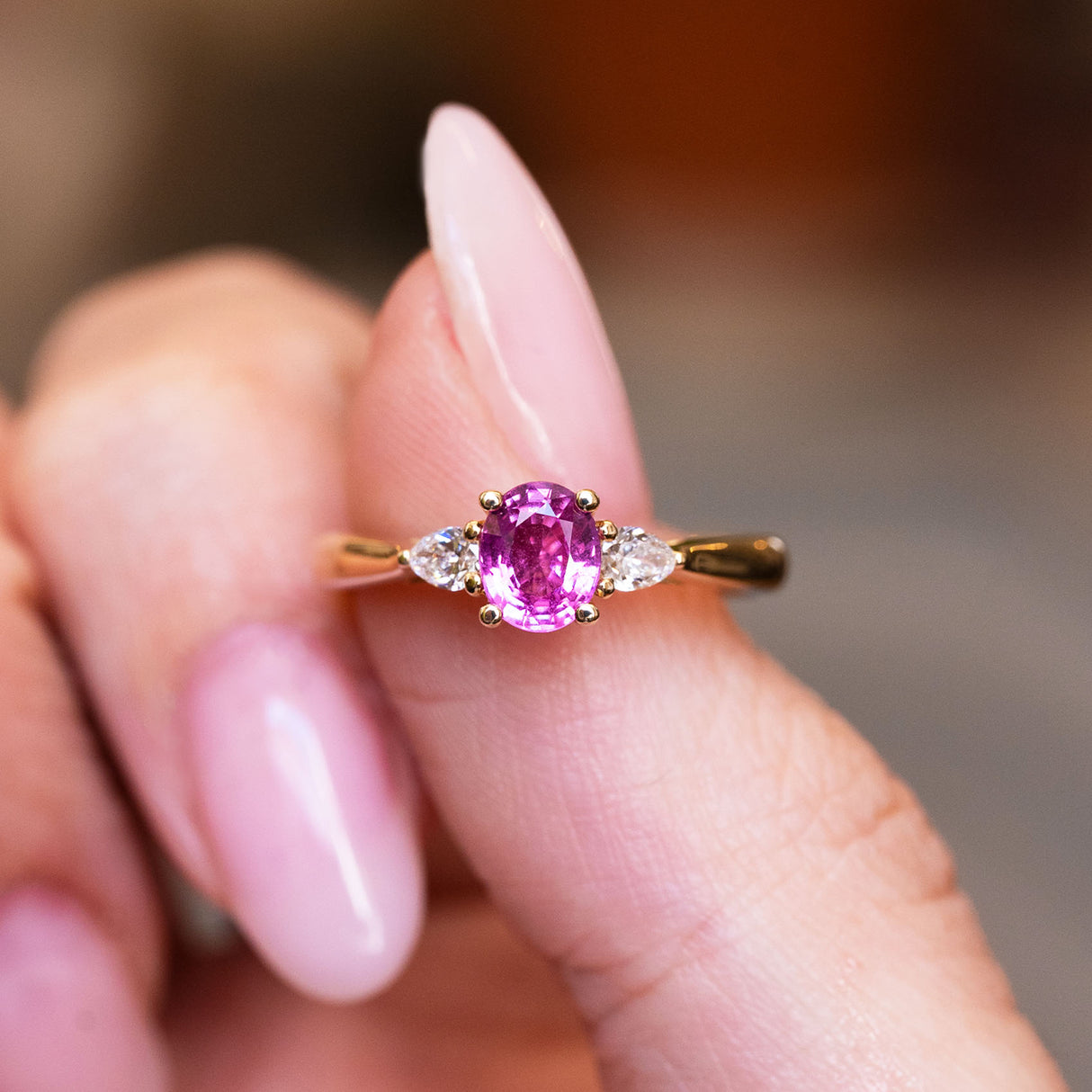 Pink oval sapphire and diamond three-stone engagement ring with oval pink sapphire centre stone.