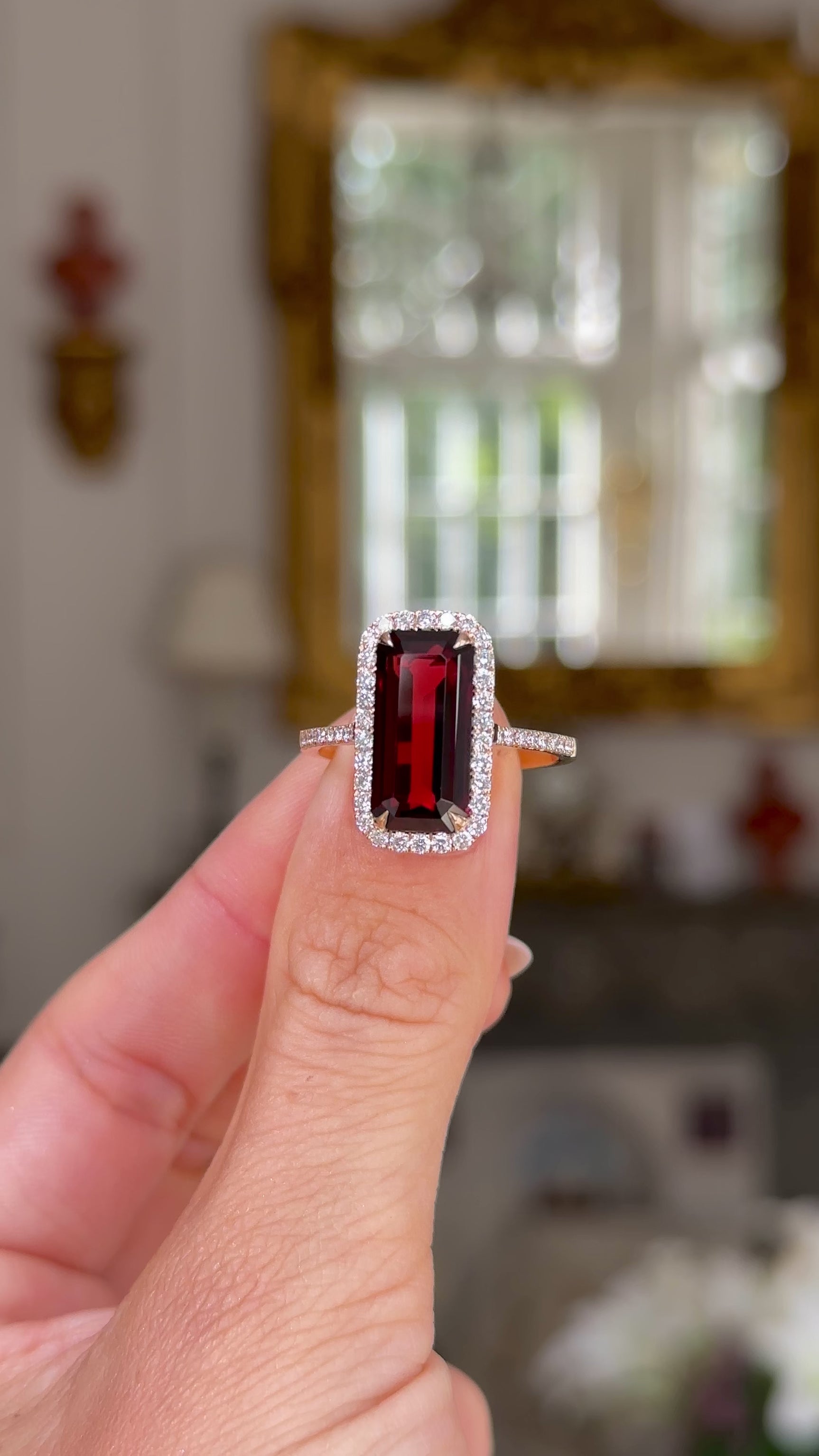 red garnet and diamond cluster ring held in fingers and rotated to give perspective.