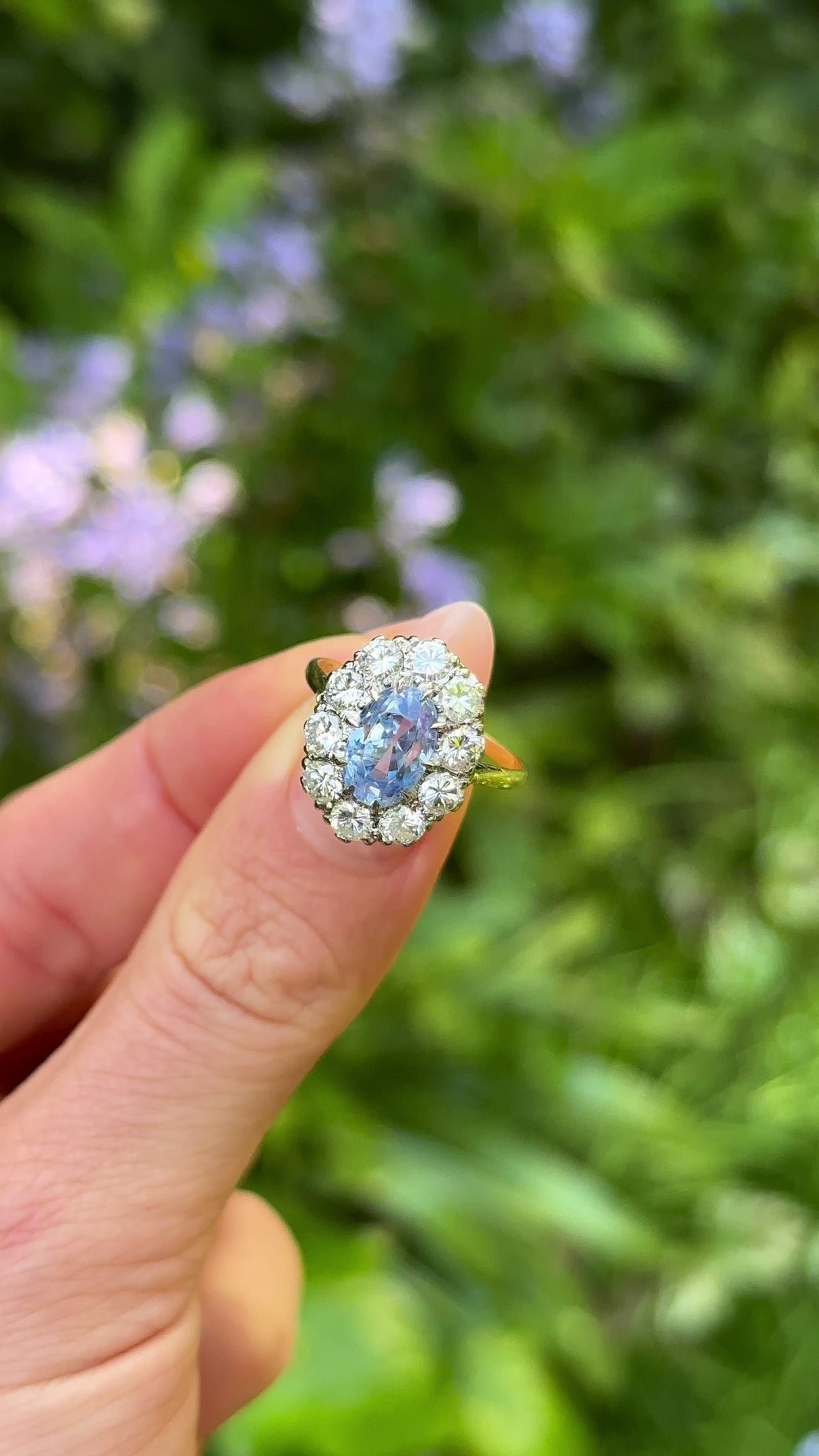 Vintage, 1980s cornflower blue sapphire & diamond cluster ring held in fingers.