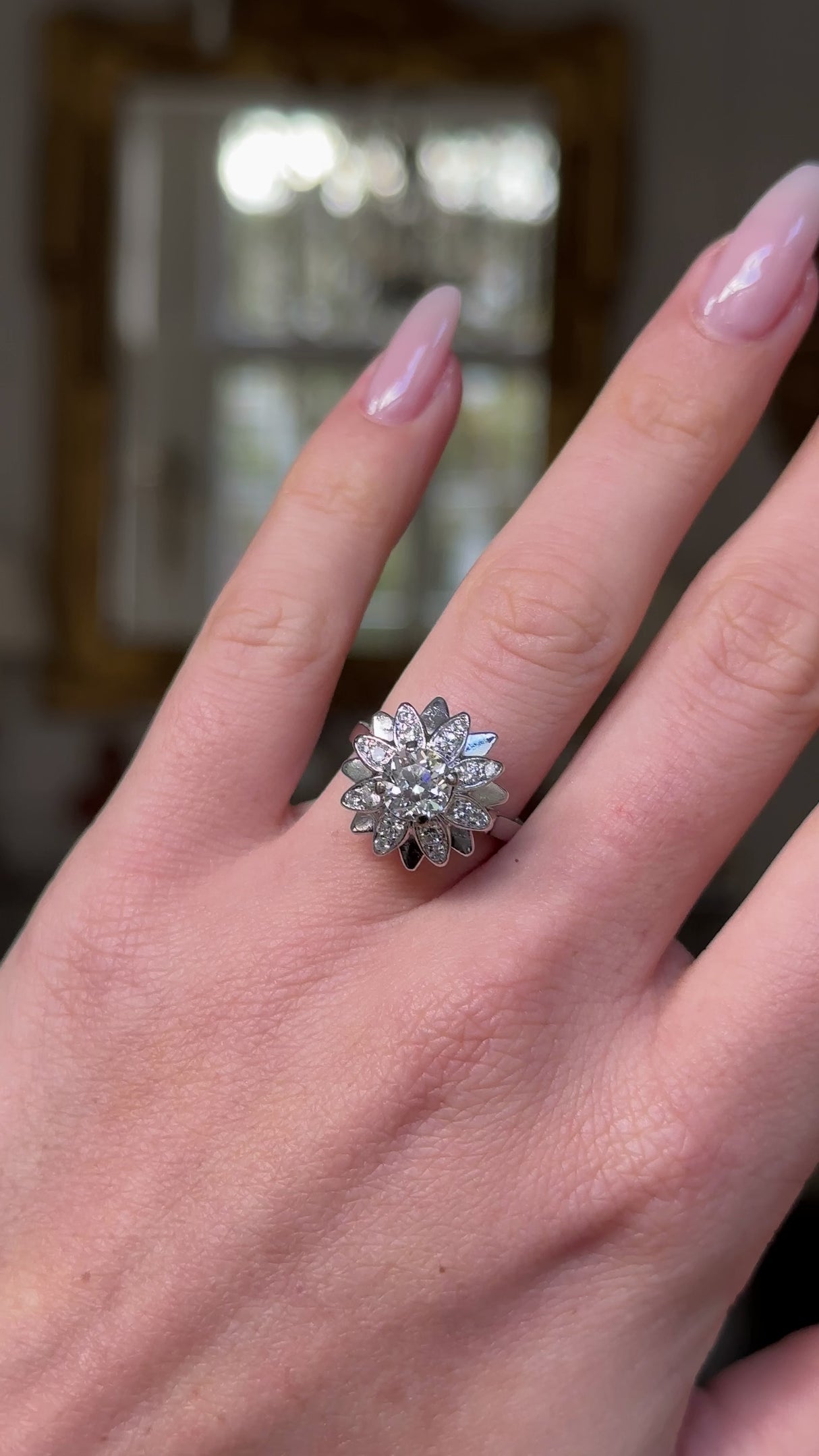 french diamond engagement ring resembling a flower worn on hand, moved away from camera to give perspective. 