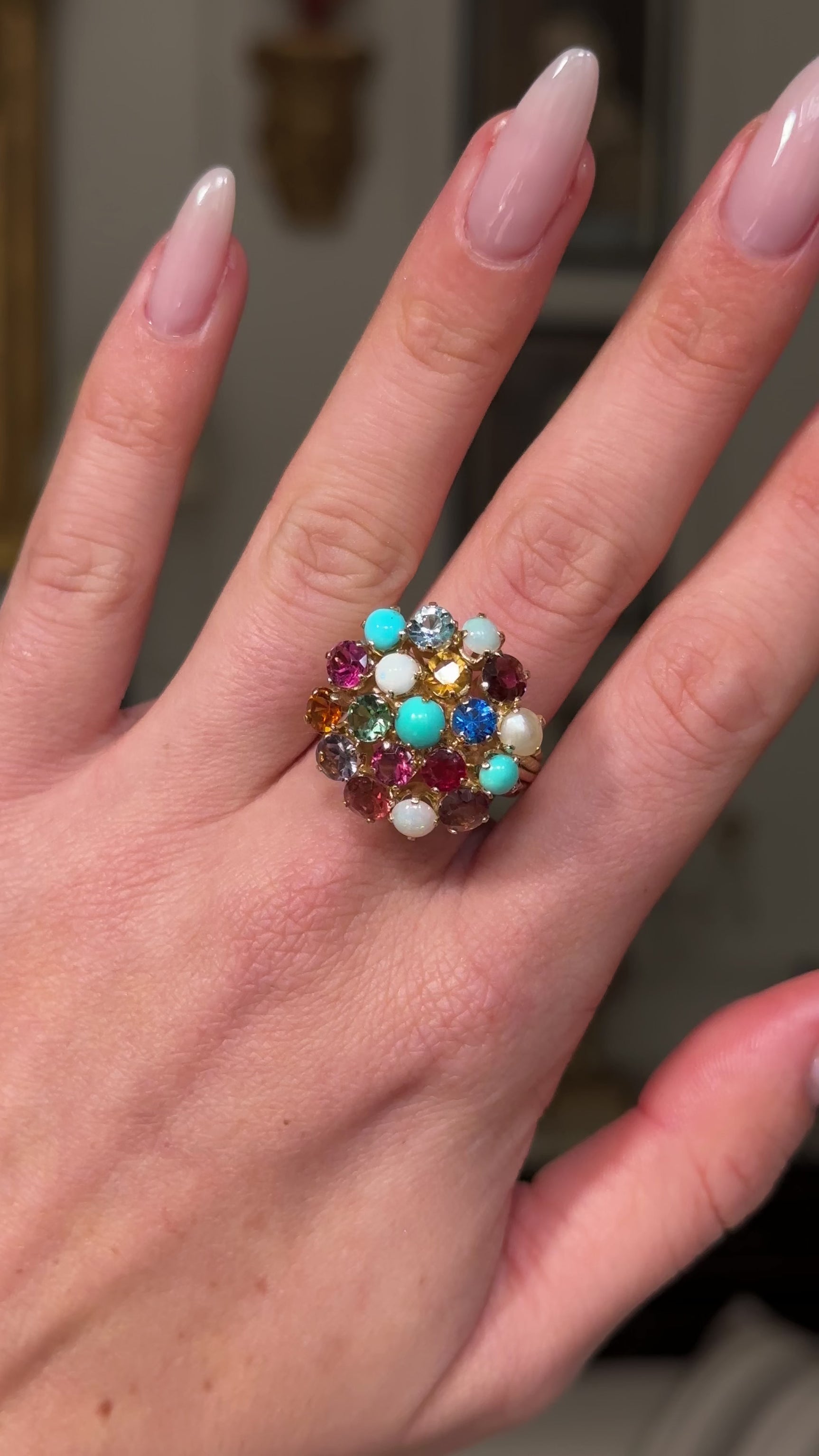 Multi gemstone cluster ring worn on hand moving  away from lens to give perspective.