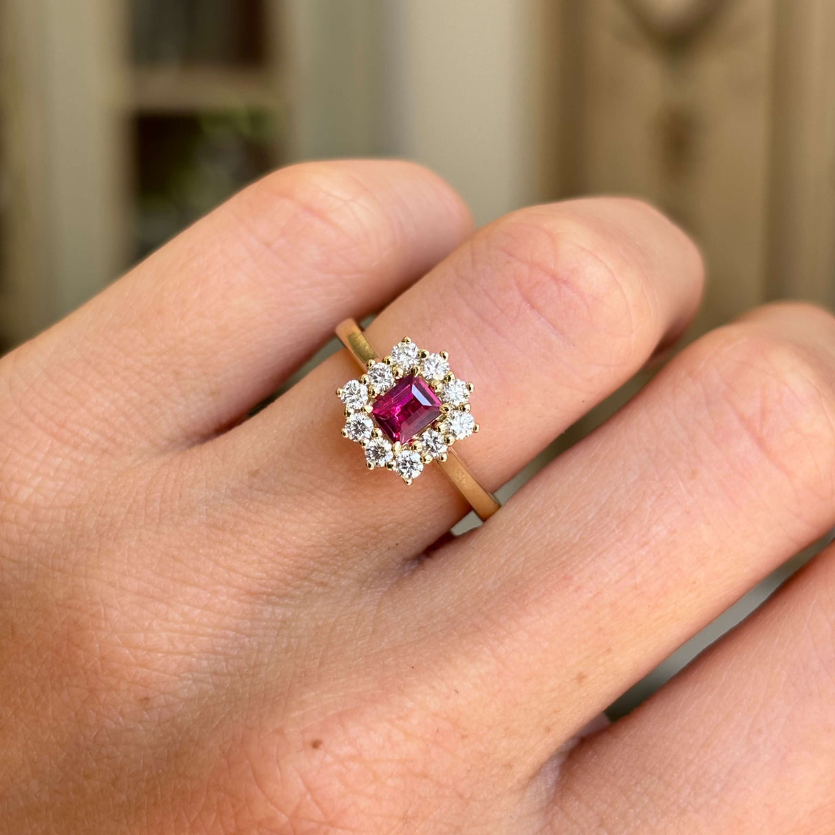 Rectangular step-cut ruby and diamond cluster engagement ring featuring a rectangular step-cut ruby encircled by diamonds, worn on a hand.