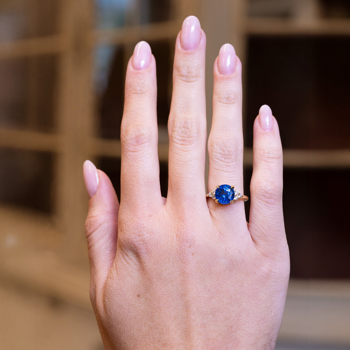 Round blue sapphire and diamond cluster tre-foil engagement ring worn on hand with vivid blue sapphire centre stone.