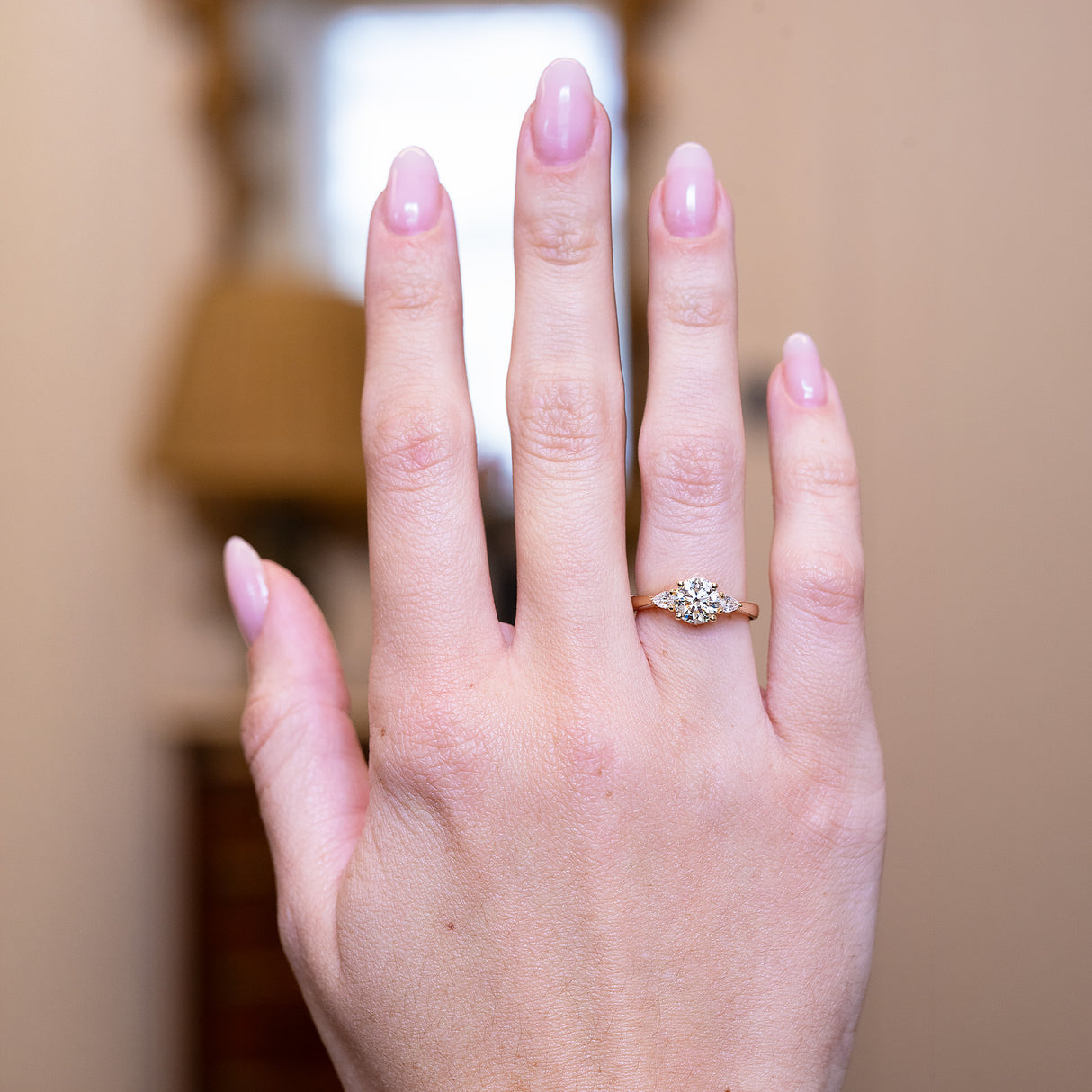 Round brilliant-cut diamond three-stone engagement ring worn on hand with tapered diamond side stones.