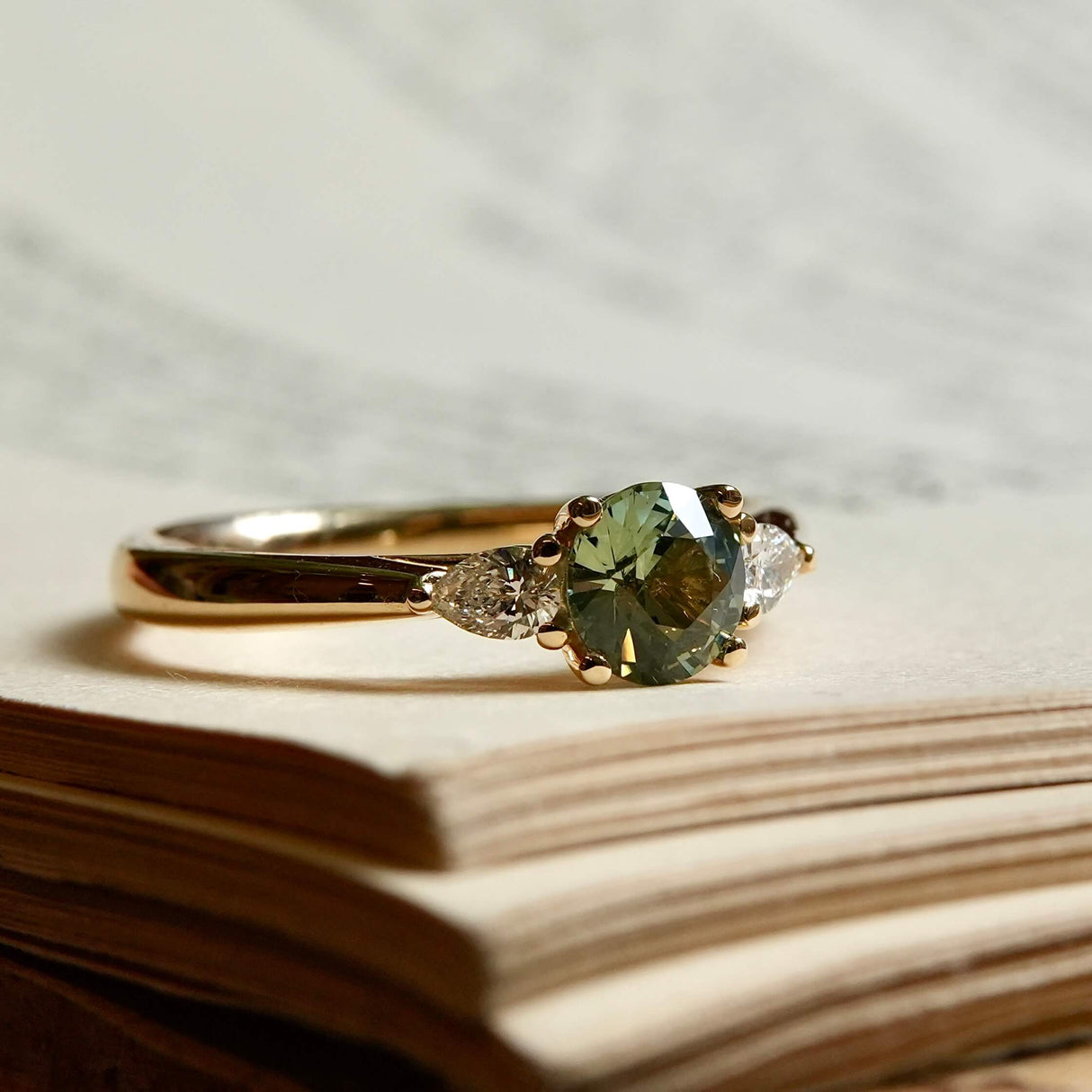Round teal sapphire and pear diamond three stone engagement ring in yellow gold