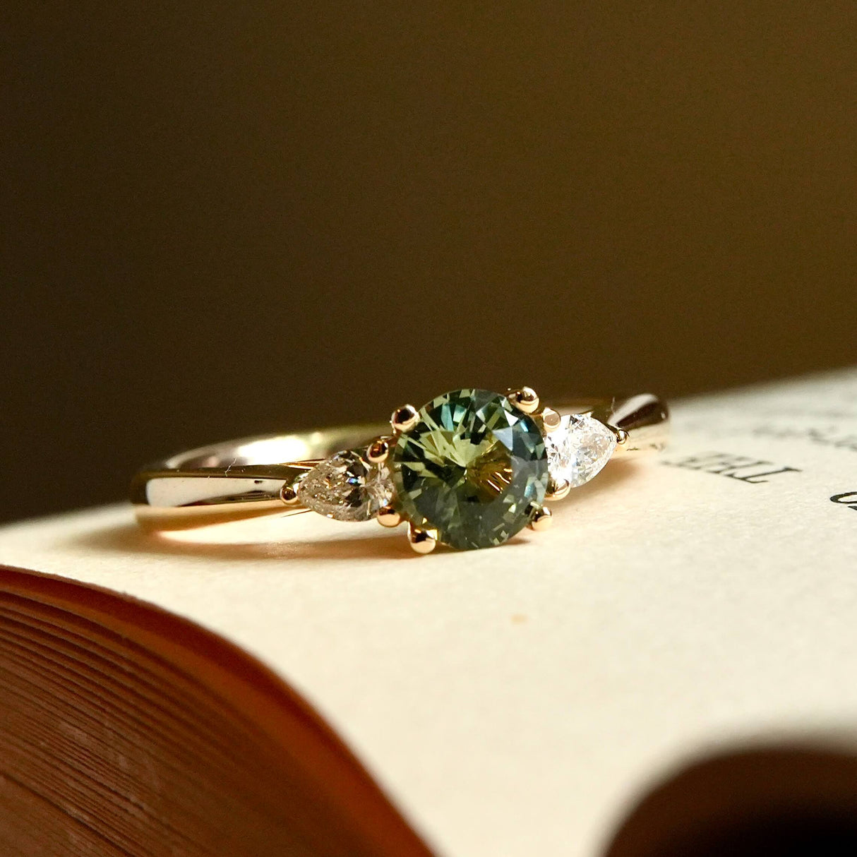 Round teal sapphire and pear diamond three stone engagement ring with yellow gold band