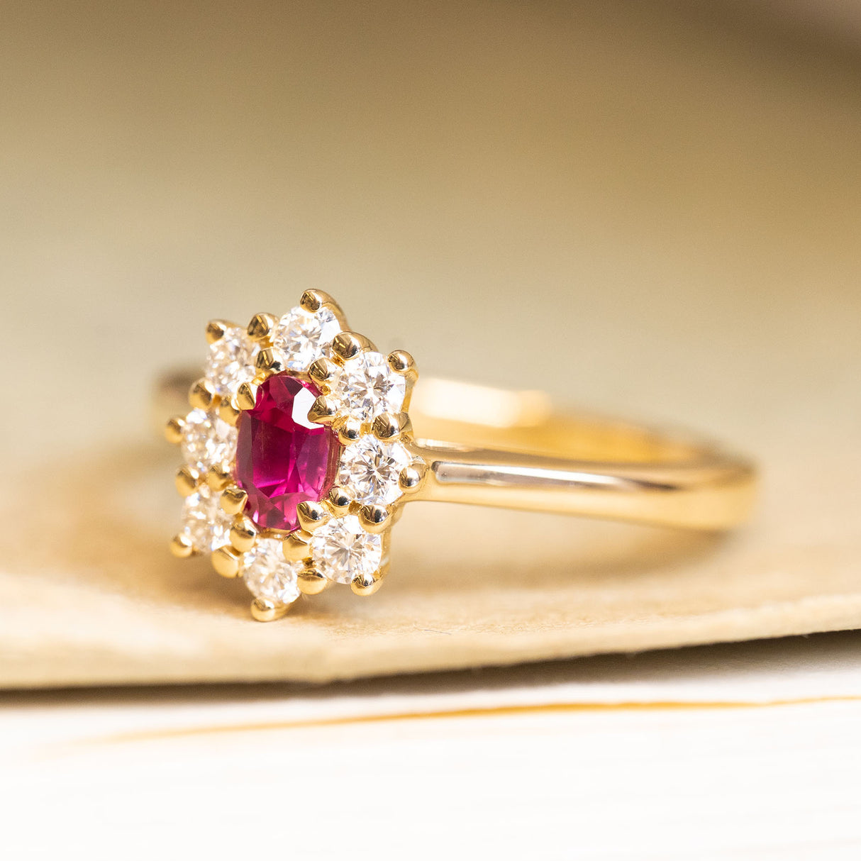 Ruby and diamond cluster engagement ring featuring a vivid red ruby surrounded by brilliant-cut diamonds in yellow gold.
