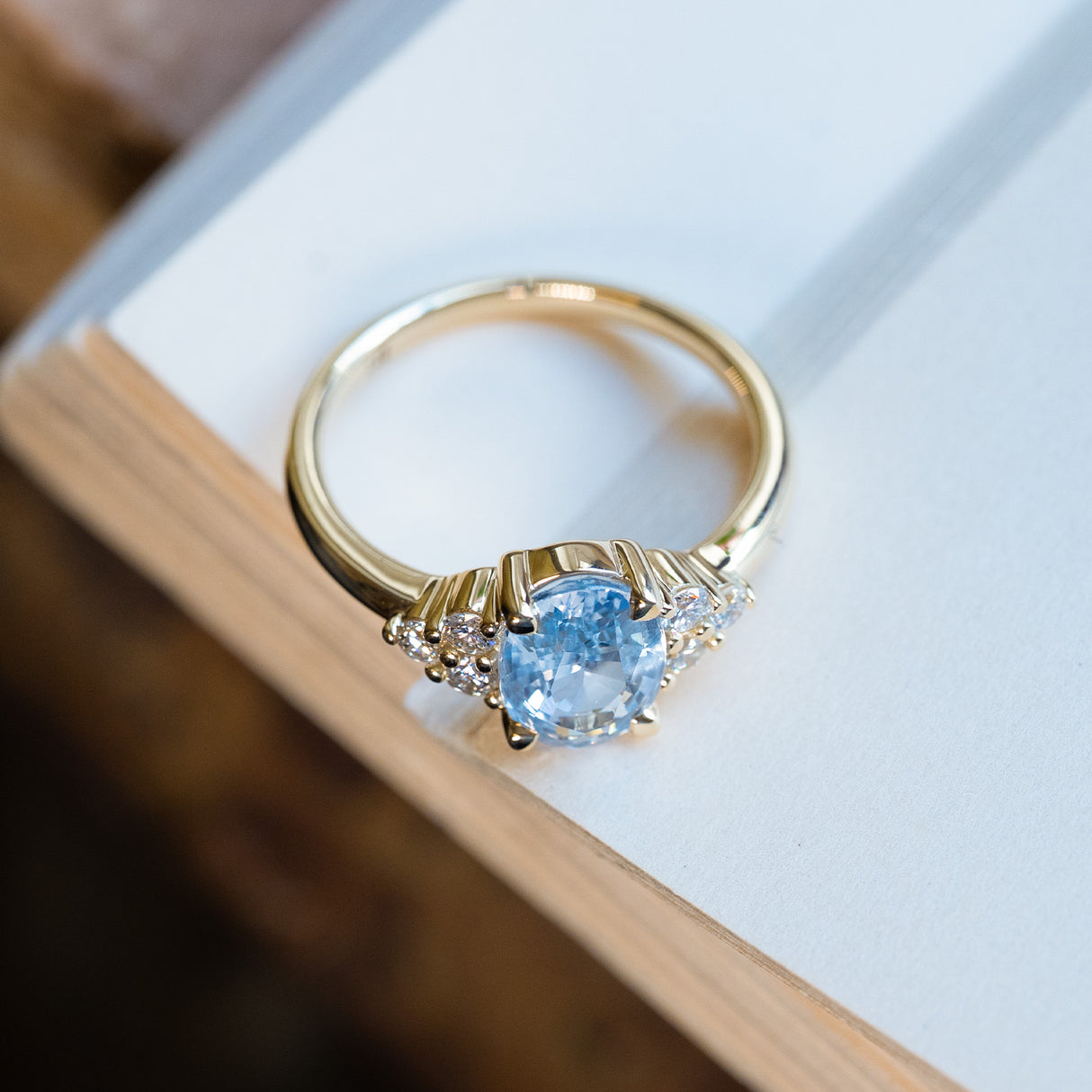 Pale blue sapphire and diamond cluster tre-foil engagement ring with elevated gallery and polished gold band.