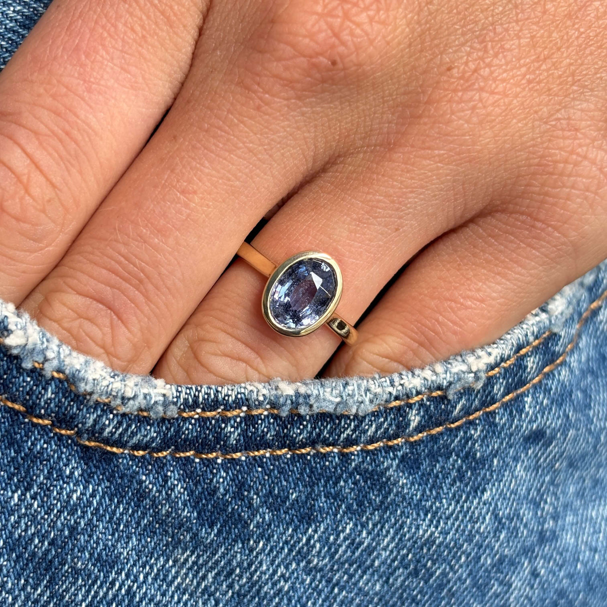 Antique-inspired yellow gold sapphire solitaire ring with an oval-cut slate blue sapphire, styled on hand against blue denim to highlight colour, scale and elegant simplicity.
