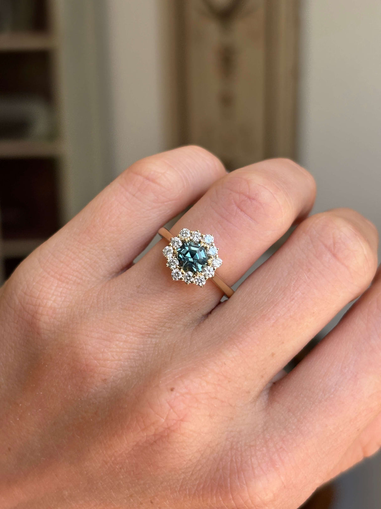 Teal hexagon-cut sapphire and diamond cluster engagement ring featuring a teal sapphire centre stone and sparkling diamond halo, worn on a hand.