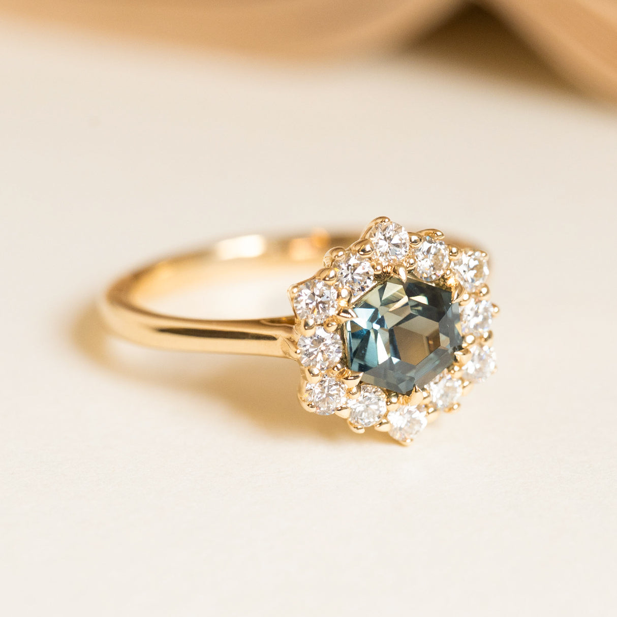 Teal sapphire engagement ring set with a hexagon-cut sapphire framed by a sparkling diamond cluster in yellow gold.