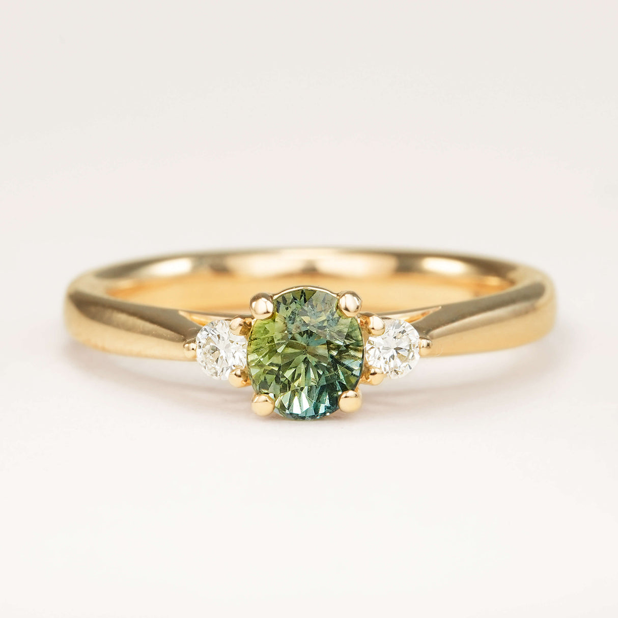 Teal sapphire and diamond three-stone engagement ring in yellow gold with round centre stone and diamond side stones.