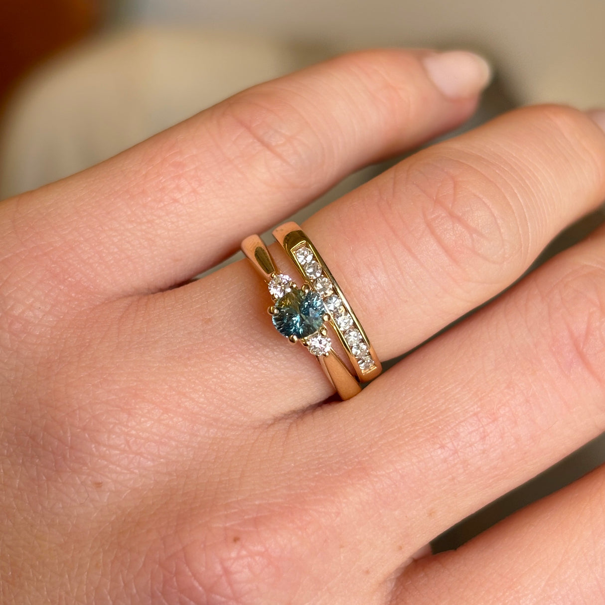 Teal sapphire three-stone engagement ring styled with diamond wedding band in yellow gold.