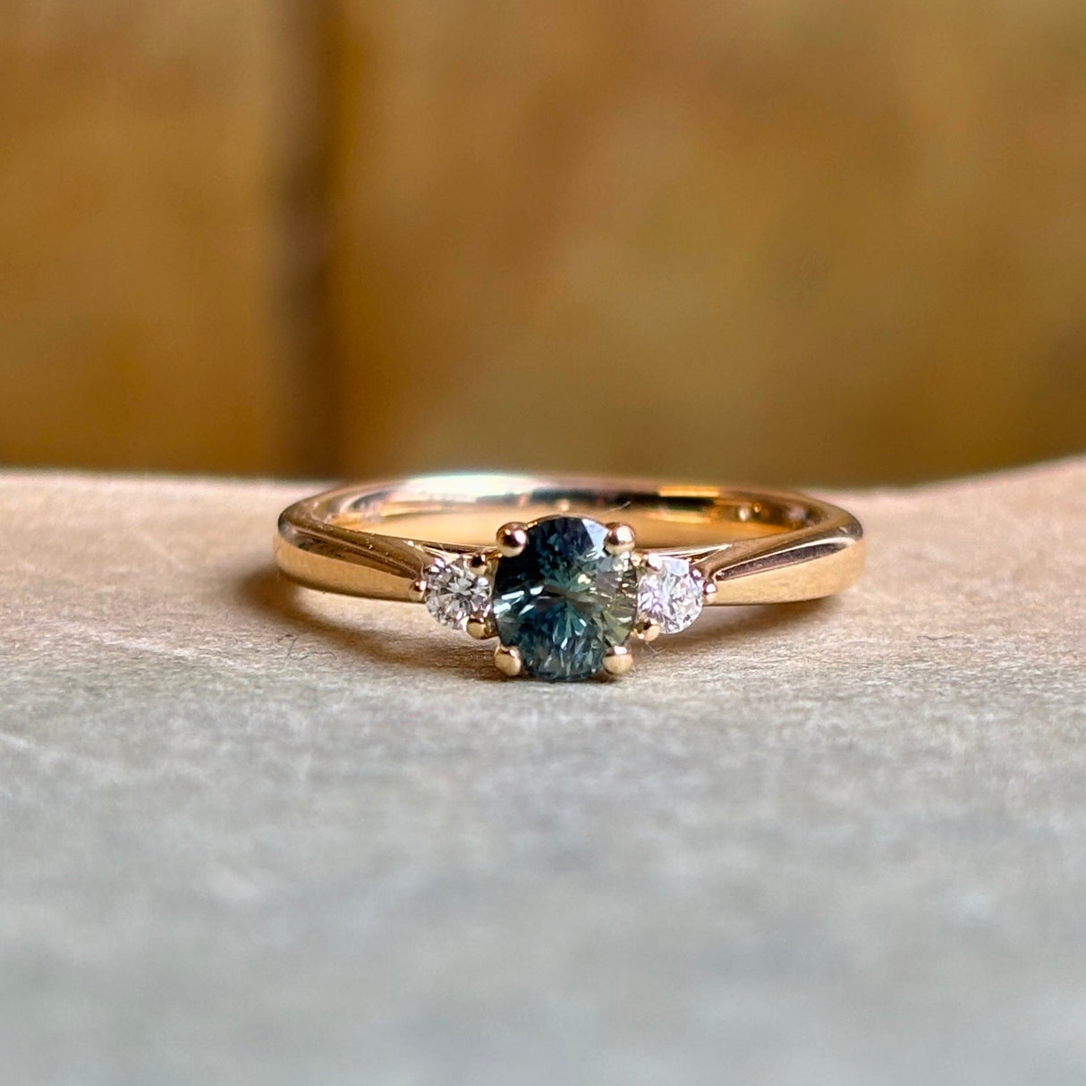 Angled view of teal sapphire engagement ring with diamond side stones in polished yellow gold.