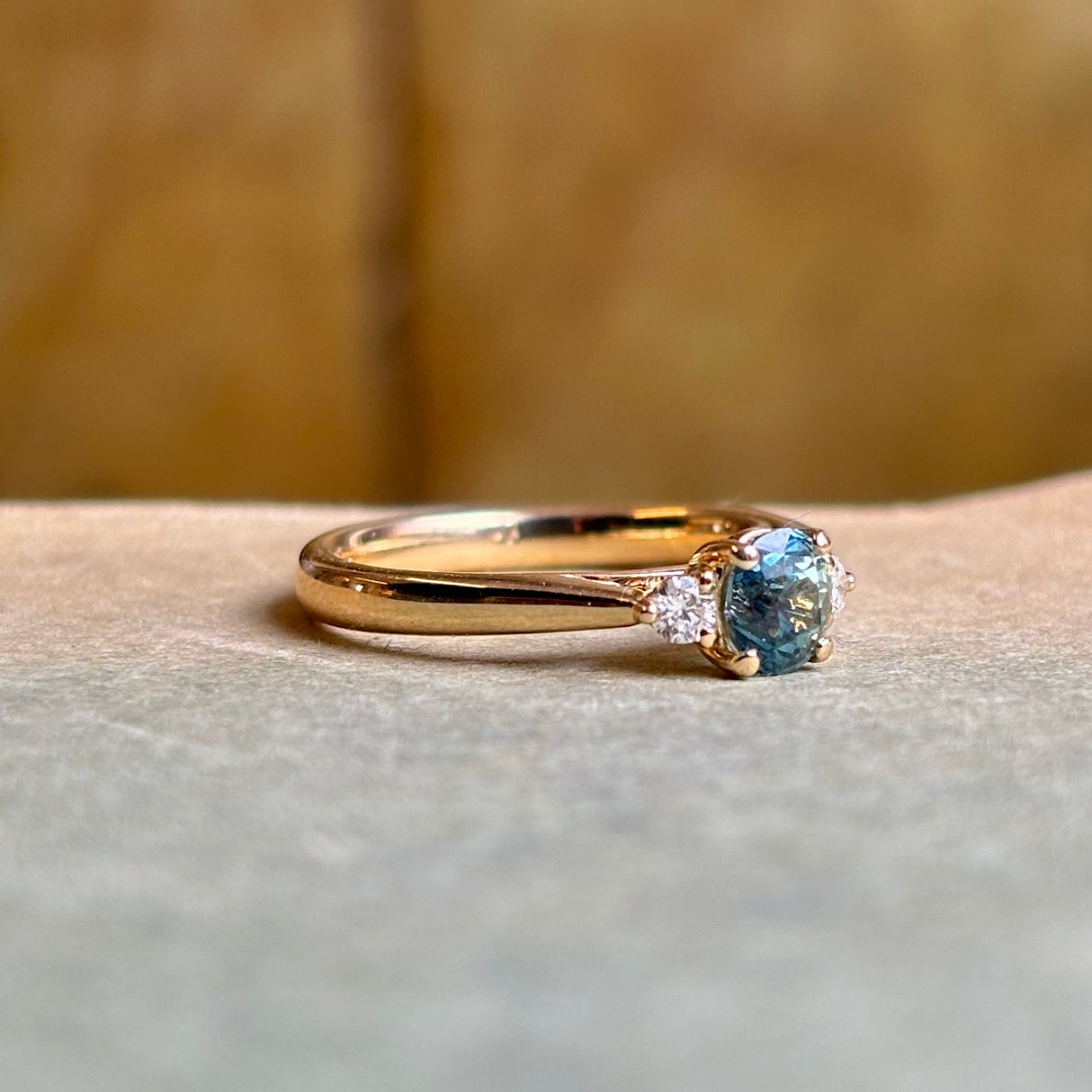 Side profile of teal sapphire and diamond three-stone engagement ring in yellow gold.
