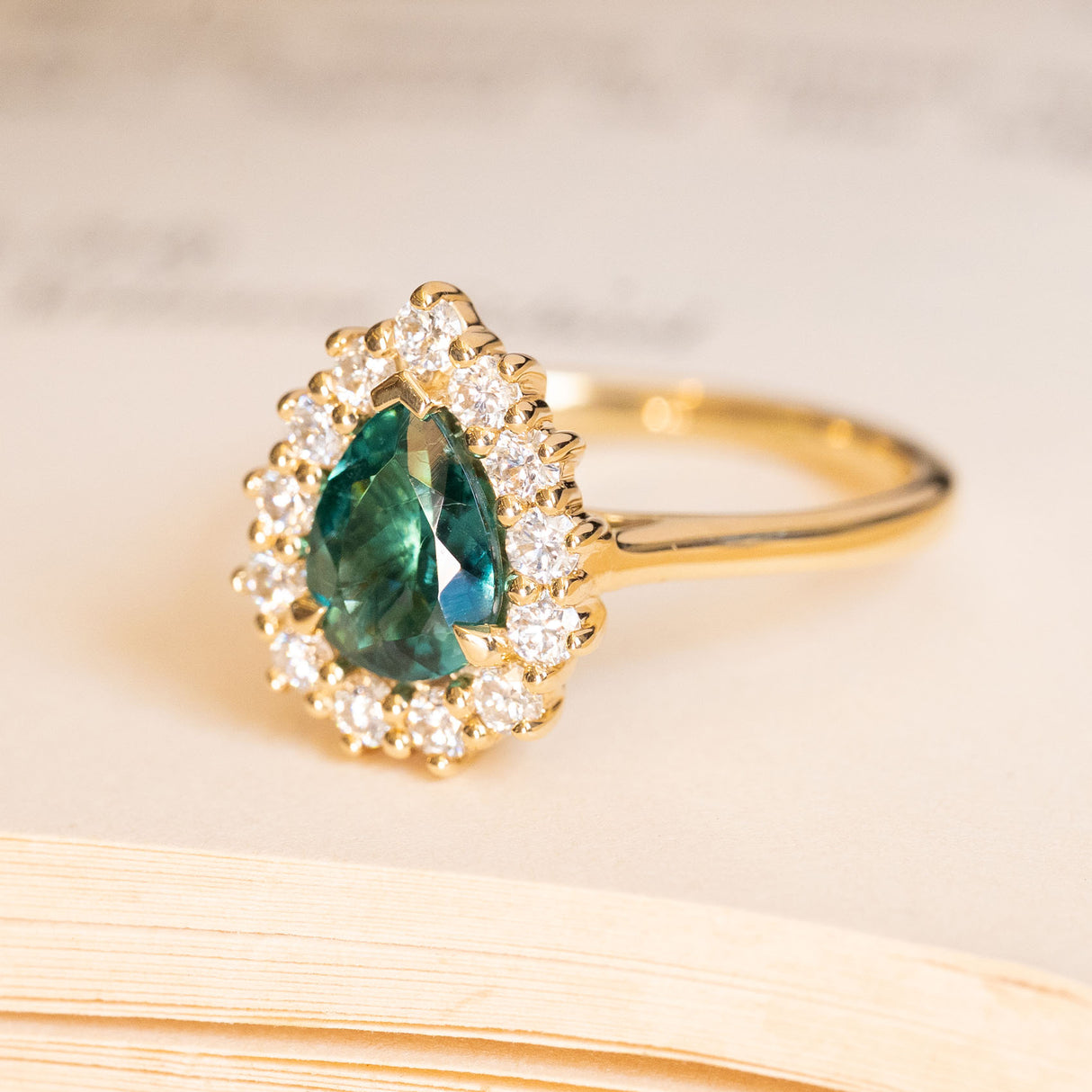 Pear-cut teal tourmaline and diamond cluster engagement ring with brilliant-cut diamond halo.