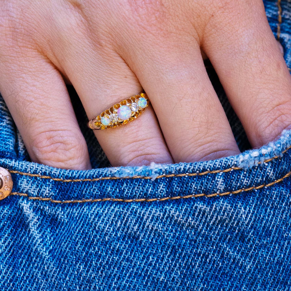 Antique opal and diamond five-stone ring styled with denim pocket.