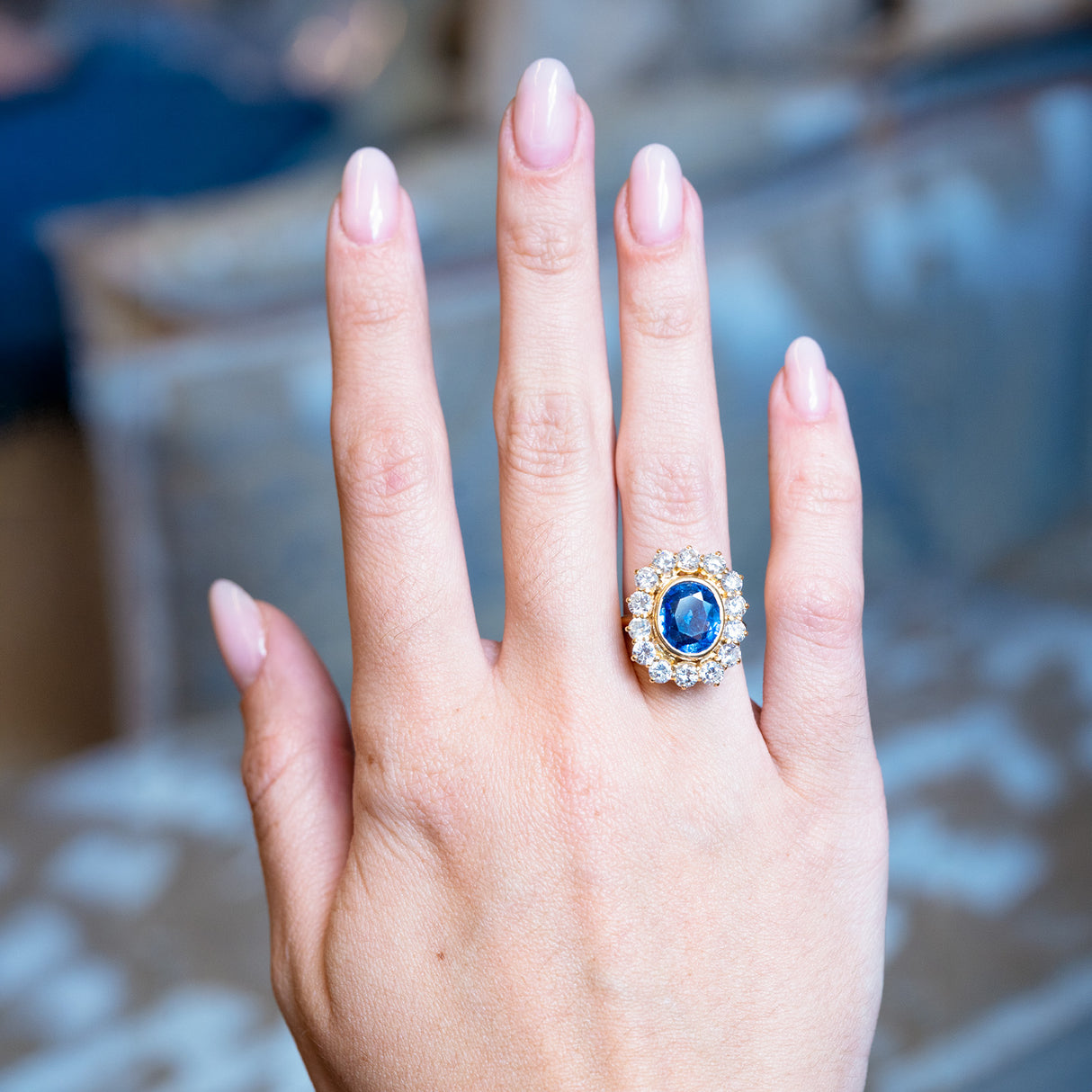 Vintage 1960s French sapphire and diamond cluster ring worn on hand with oval blue sapphire and diamond halo.