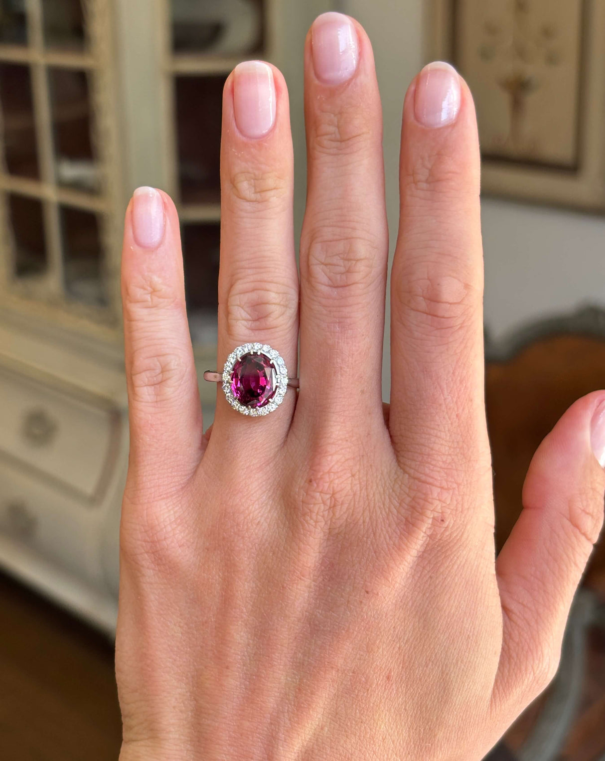 Vintage 1960s garnet and diamond cluster engagement ring with an oval garnet centre stone and diamond halo, displayed on a hand.