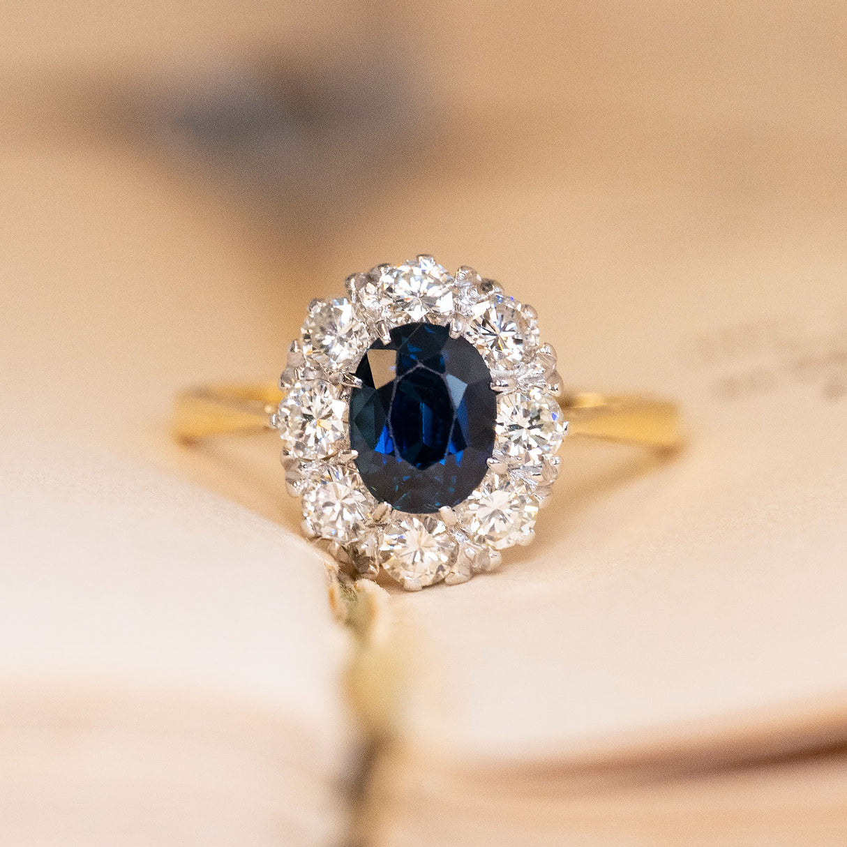 Vintage 1960s sapphire and diamond cluster ring featuring an oval-cut blue sapphire surrounded by a cluster of brilliant-cut diamonds in yellow gold.