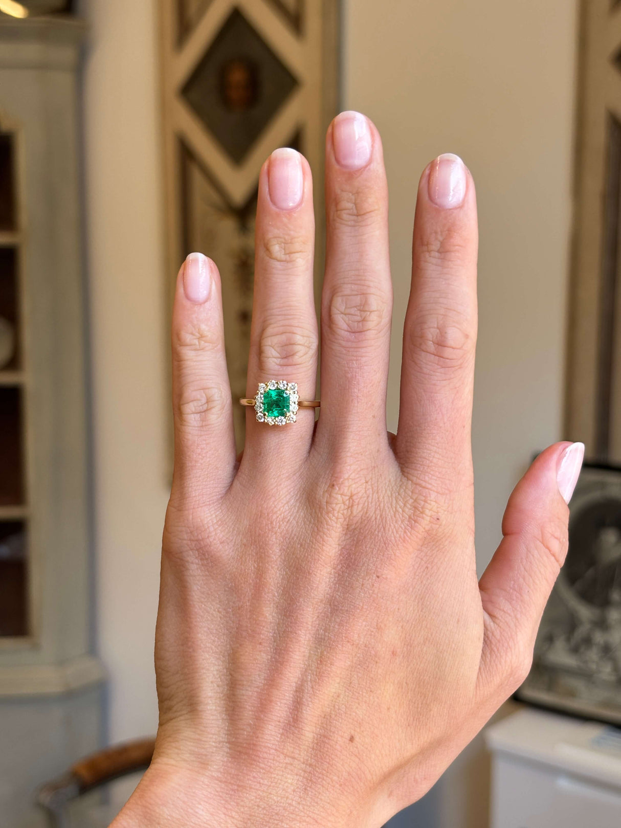 Vintage 1980s Colombian emerald and diamond cluster engagement ring with an emerald-cut Colombian emerald and diamond halo, displayed on a hand.