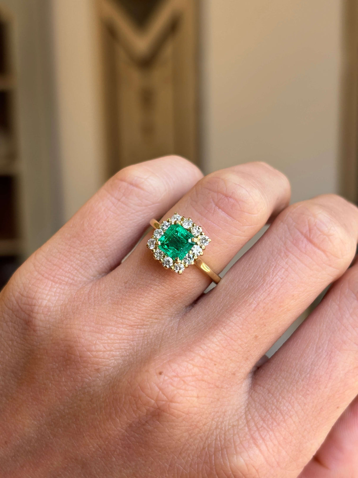 Vintage 1980s Colombian emerald and diamond cluster engagement ring featuring an emerald-cut Colombian emerald encircled by brilliant-cut diamonds, worn on a hand.