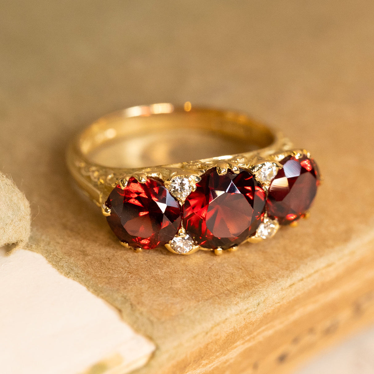 Vintage yellow gold garnet three-stone ring showcasing deep red garnets with sparkling diamond accents and carved shoulders.
