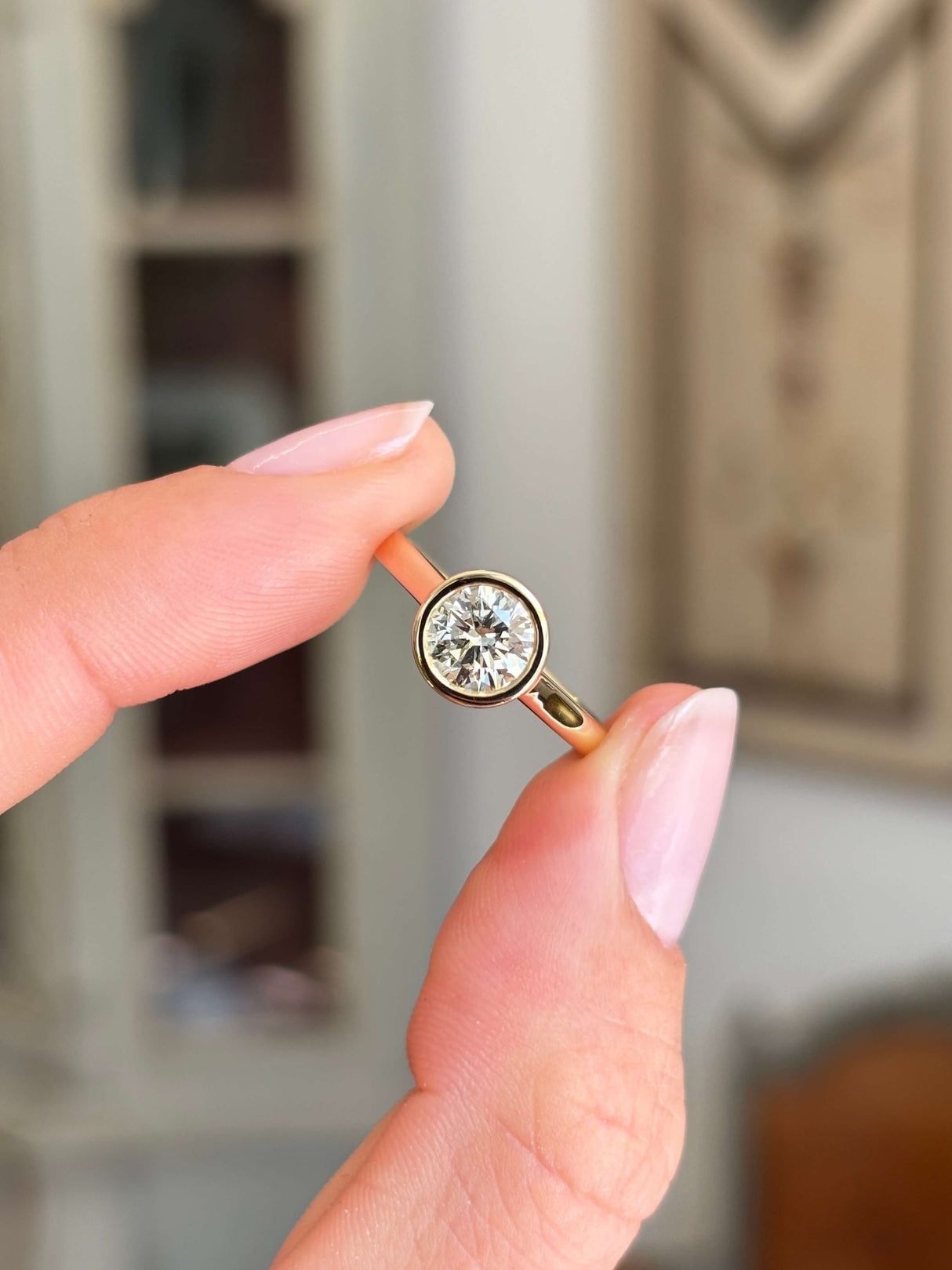 Vintage inspired diamond rub-over solitaire engagement ring with a round brilliant-cut diamond in a classic rub-over setting, held by hand.