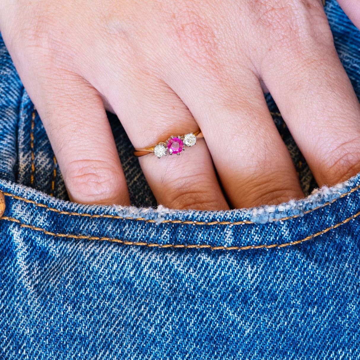 Vintage ruby and diamond three-stone ring worn with denim pocket styling.